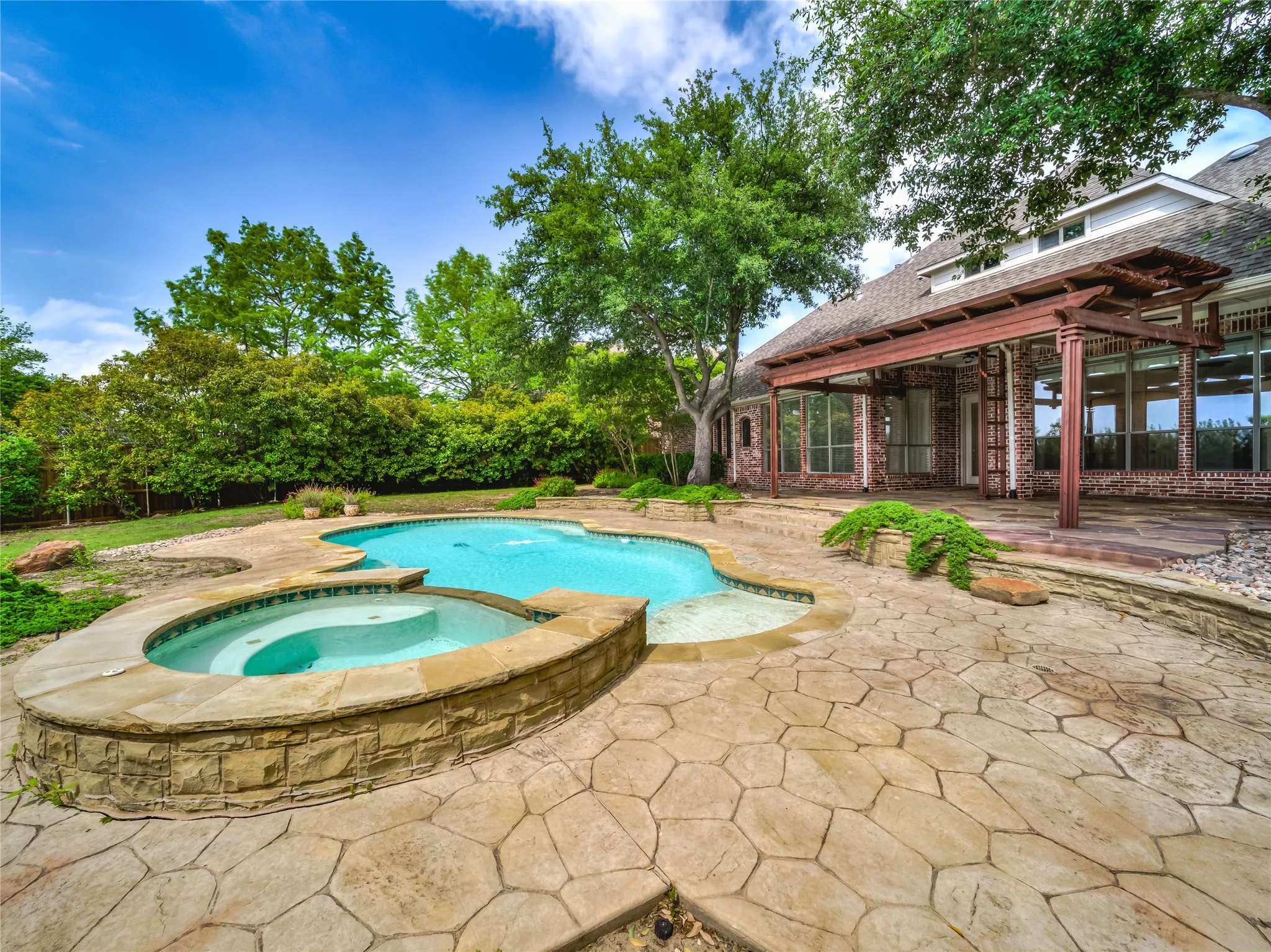 Resort-style backyard featuring a freeform swimming pool with integrated spa, extensive stamped concrete patio, and a covered pergola