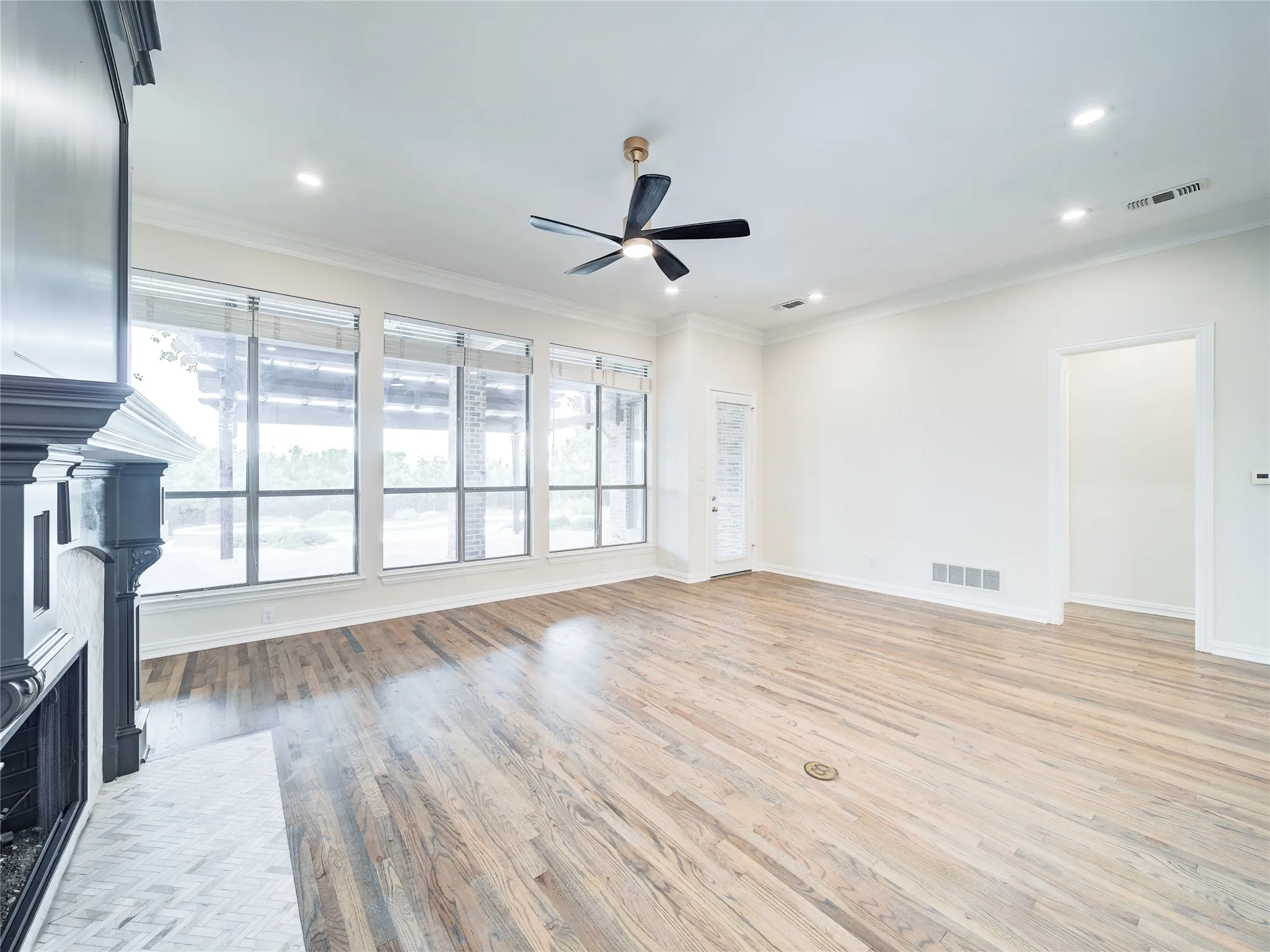 Spacious room featuring wood-finish flooring, a decorative fireplace with herringbone tile hearth, and a wall of windows
