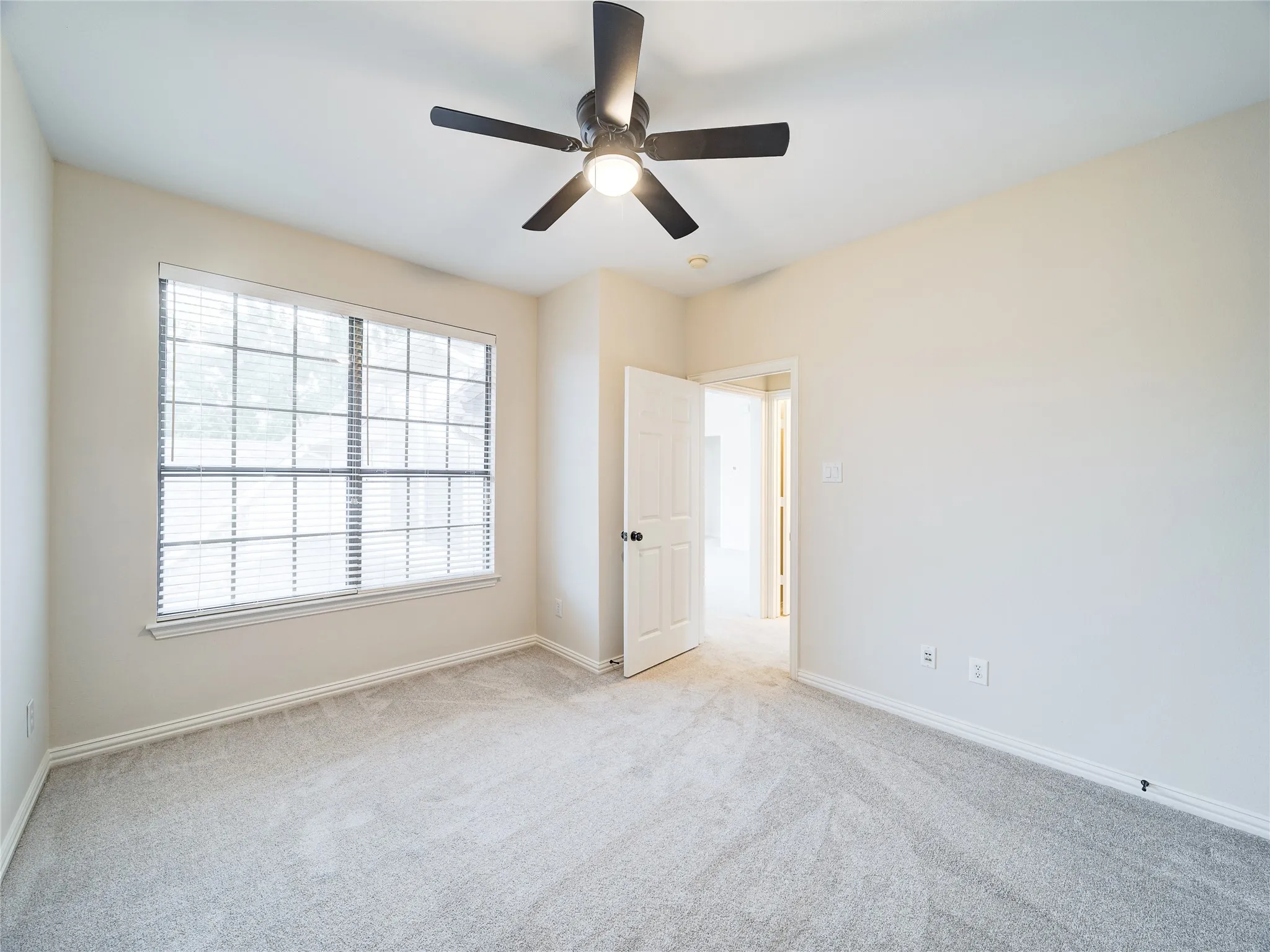 Bright room featuring light-toned carpeting, a multi-pane window with horizontal blinds, and a dark-toned ceiling fan with integrated lighting