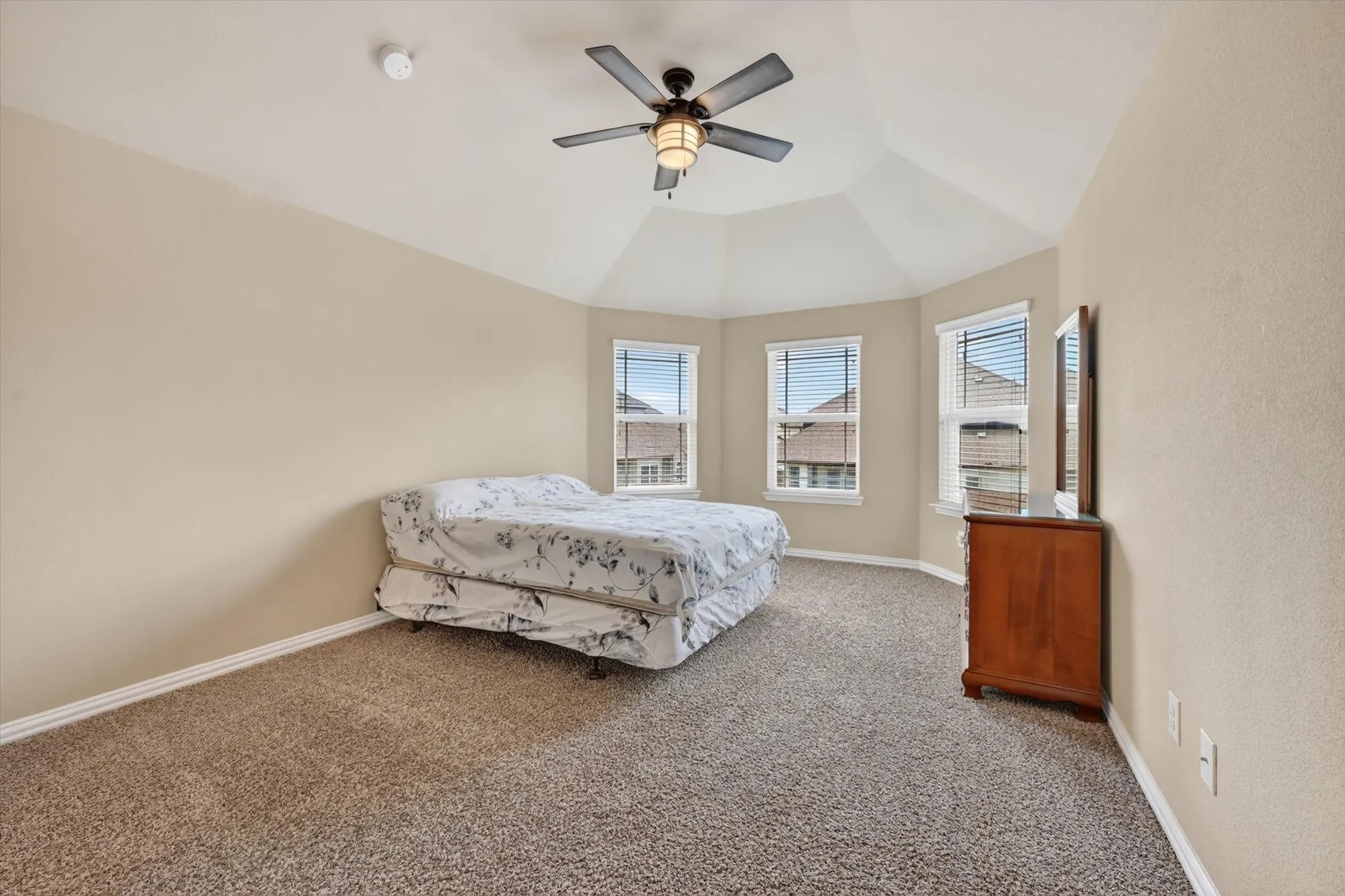 Room featuring a vaulted ceiling with a ceiling fan, three windows with blinds, and neutral-toned wall-to-wall carpeting