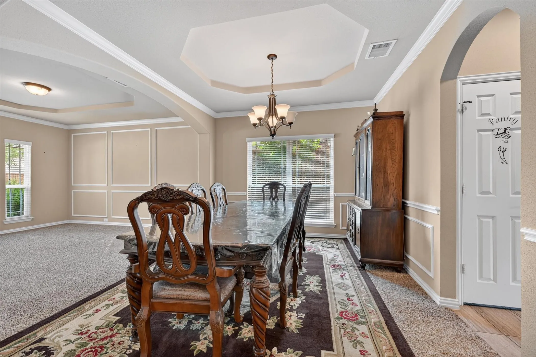 Dining area with tray ceiling, chandelier lighting, decorative wall molding, window with blinds, and an arched entryway