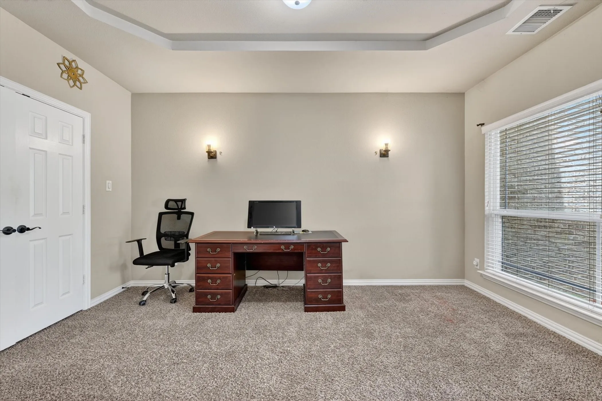 Carpeted room featuring a window with blinds, tray ceiling, and a paneled door with dark hardware