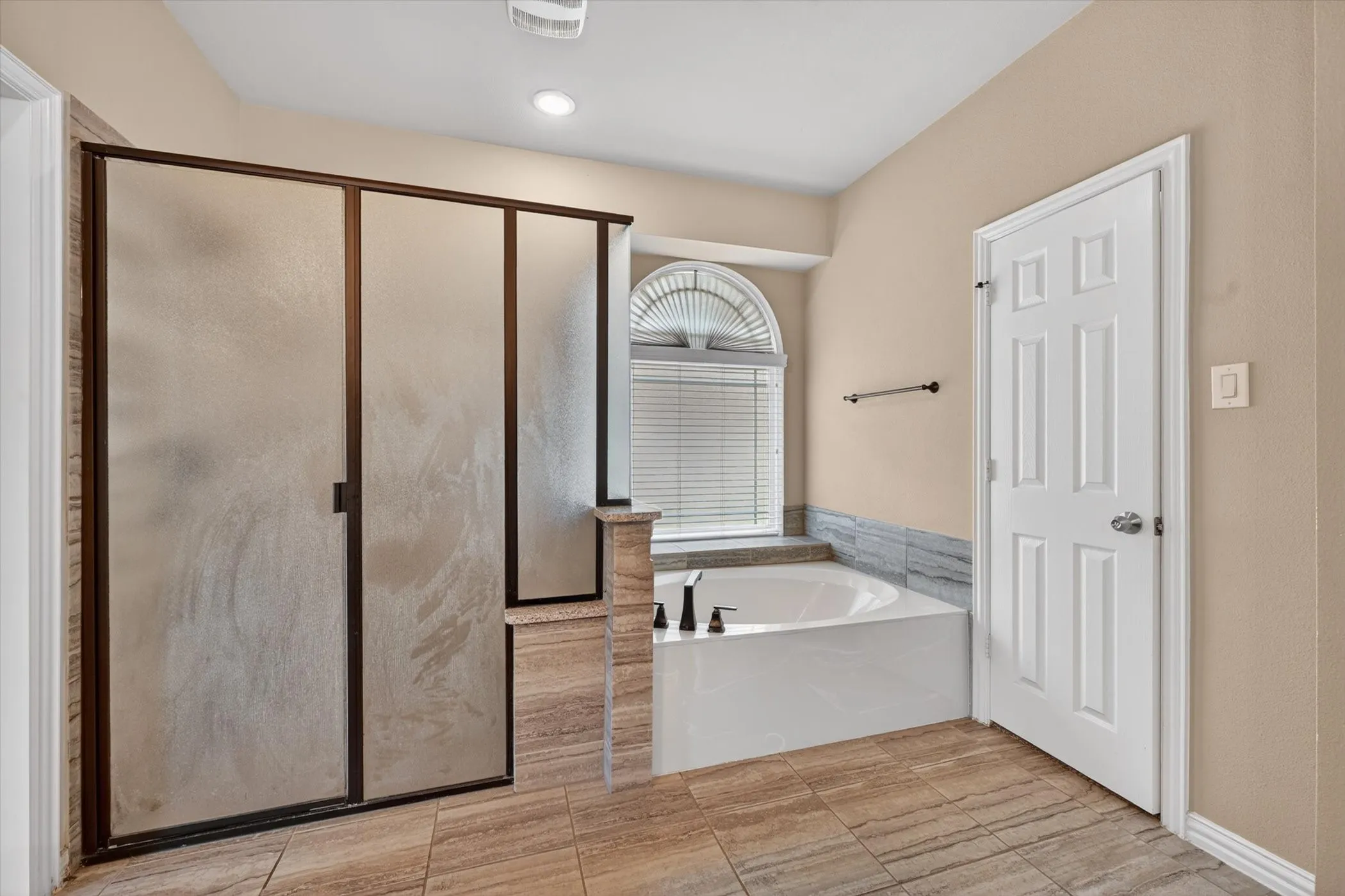 Bathroom featuring a frosted glass shower enclosure, a built-in tub with a tiled surround, a window with an arched transom, tiled flooring, and a paneled interior door