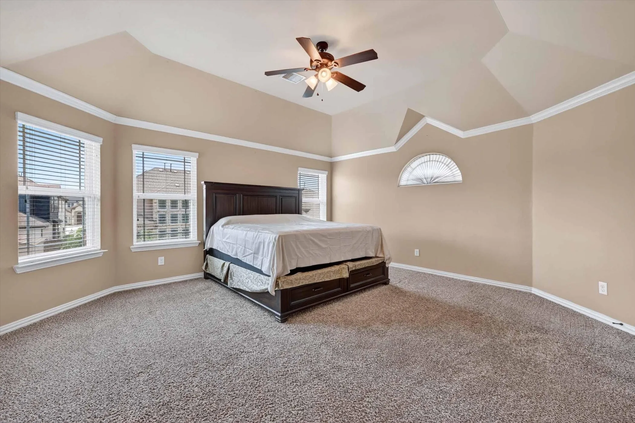 Spacious bedroom featuring vaulted ceilings, crown molding, a ceiling fan, and multiple windows with blinds