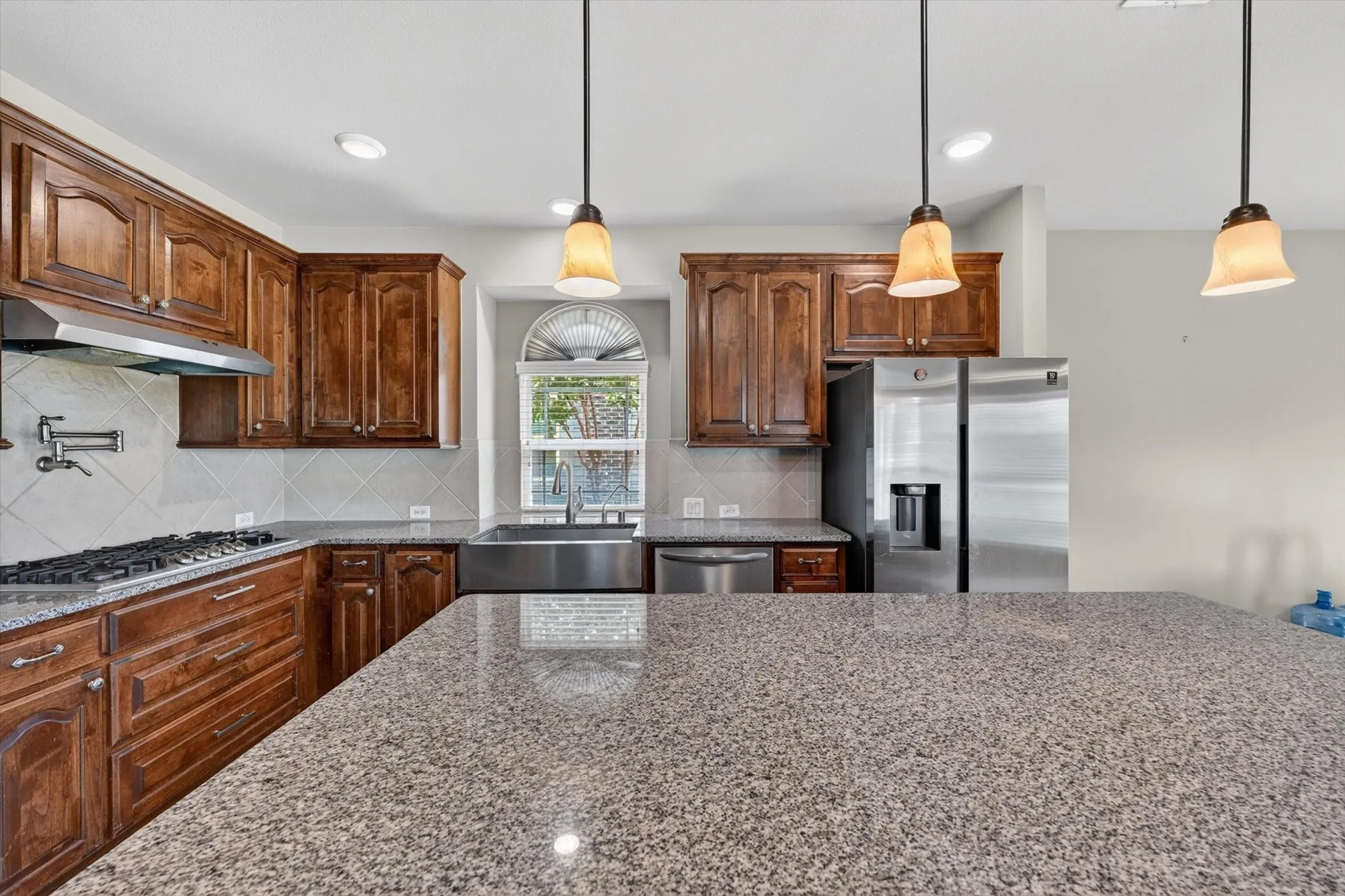 Kitchen featuring granite countertops, wood cabinetry, stainless steel appliances, and pendant lighting