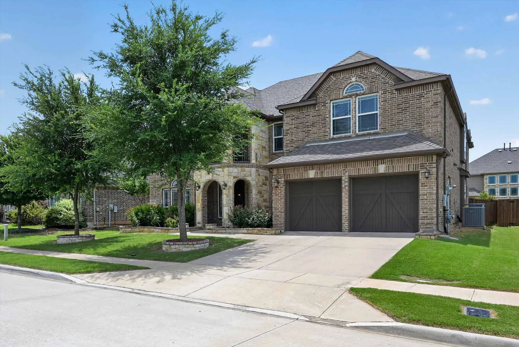 Brick and stone façade featuring an arched entry, two-car garage with carriage-style doors, symmetrical front landscaping, and a concrete driveway