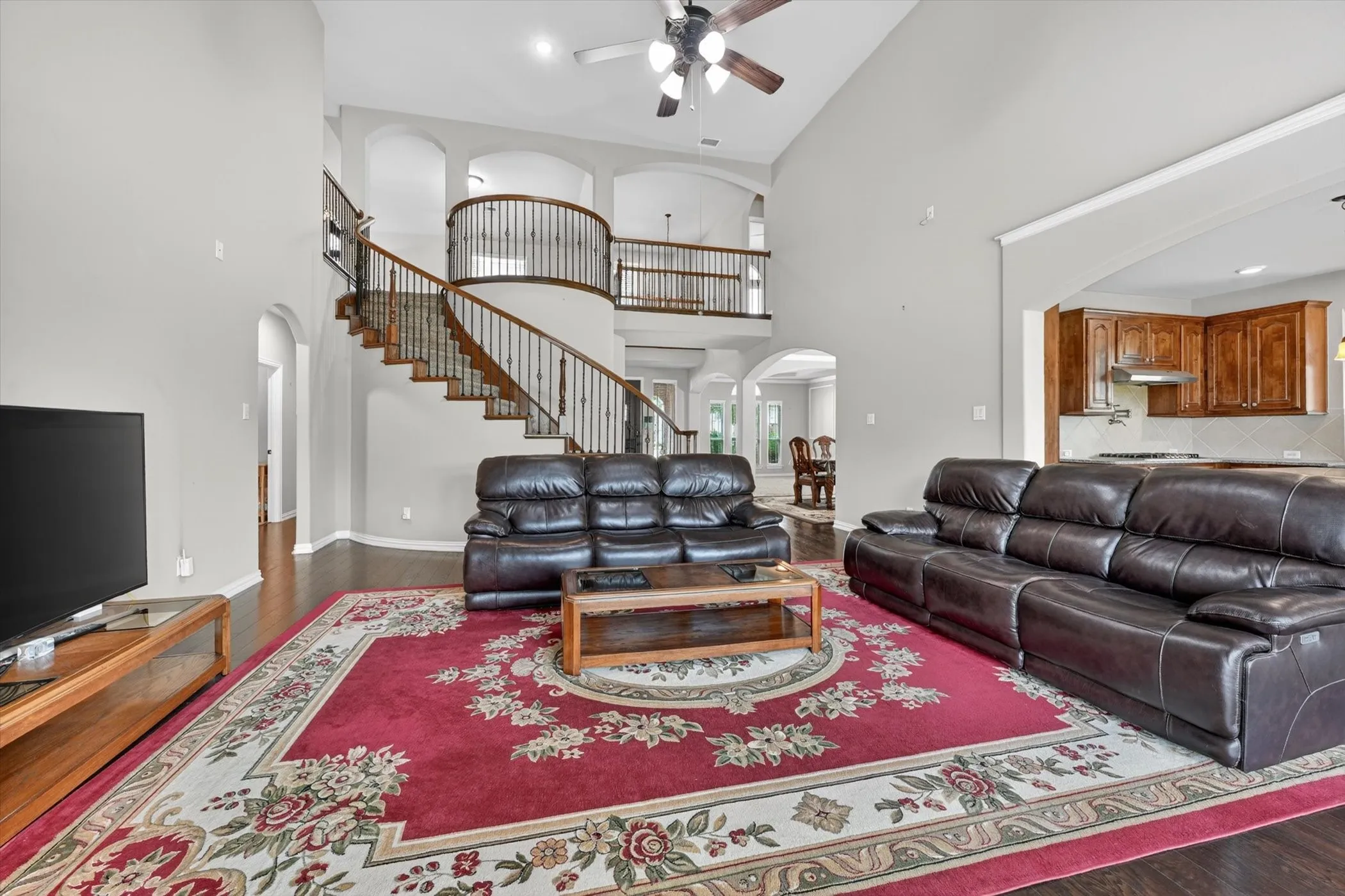 Two-story living area featuring wood-finish flooring, a grand curved staircase with wrought iron balusters, and a second-story landing with matching balusters