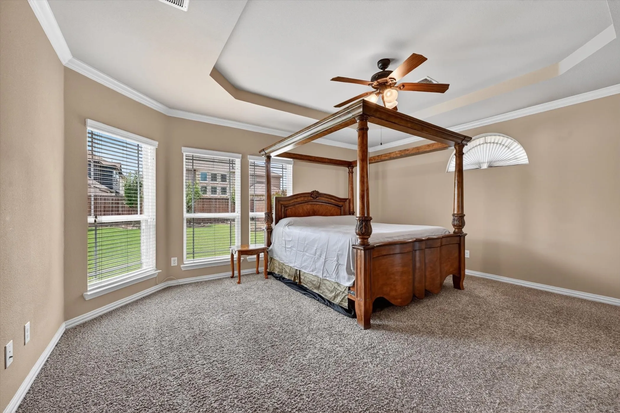 Carpeted room featuring a ceiling fan, tray ceiling, and a bay window with multiple vertical windows