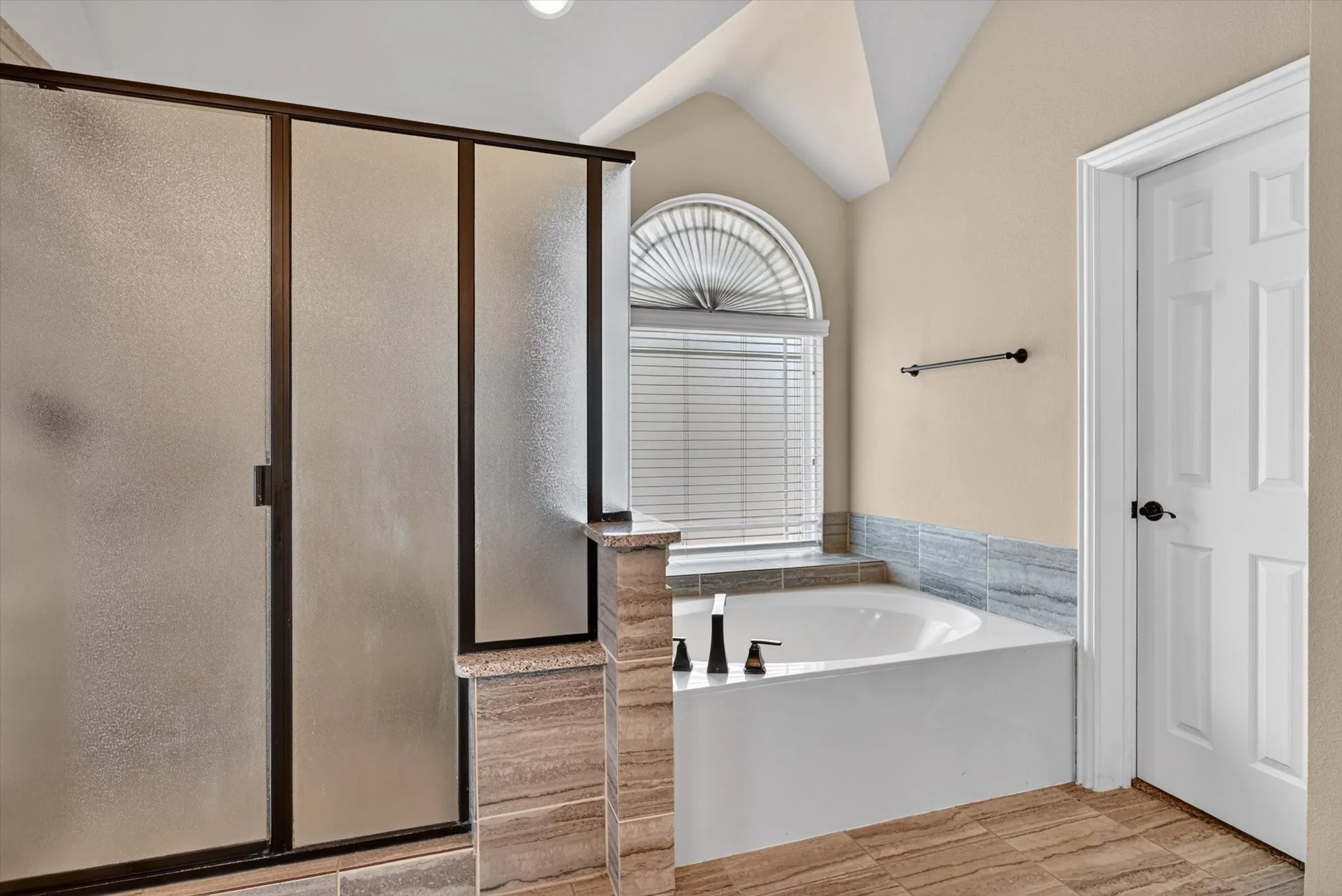 Spacious bathroom featuring a frameless shower enclosure with frosted glass panels, a separate soaking tub, and a window with arched transom