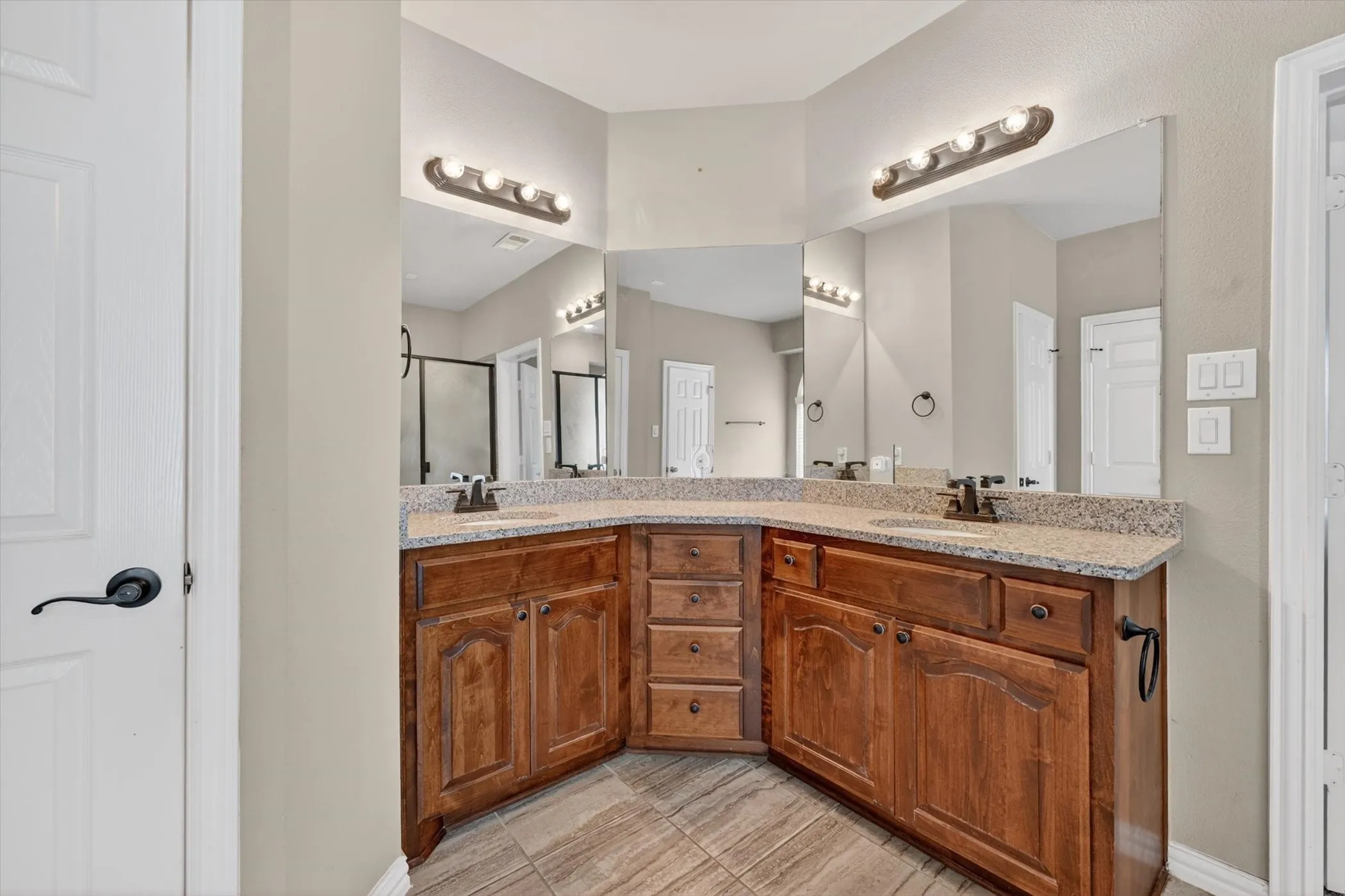 Bathroom featuring a corner double vanity with wood cabinetry, light-colored countertops, dual undermount sinks, and bronze-finish faucets