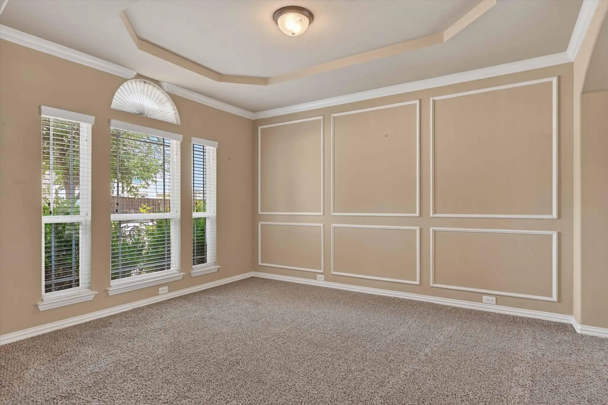 Spacious interior room featuring carpet flooring, tray ceiling, decorative wall molding, a multi-window arrangement with an arched transom, and crown molding