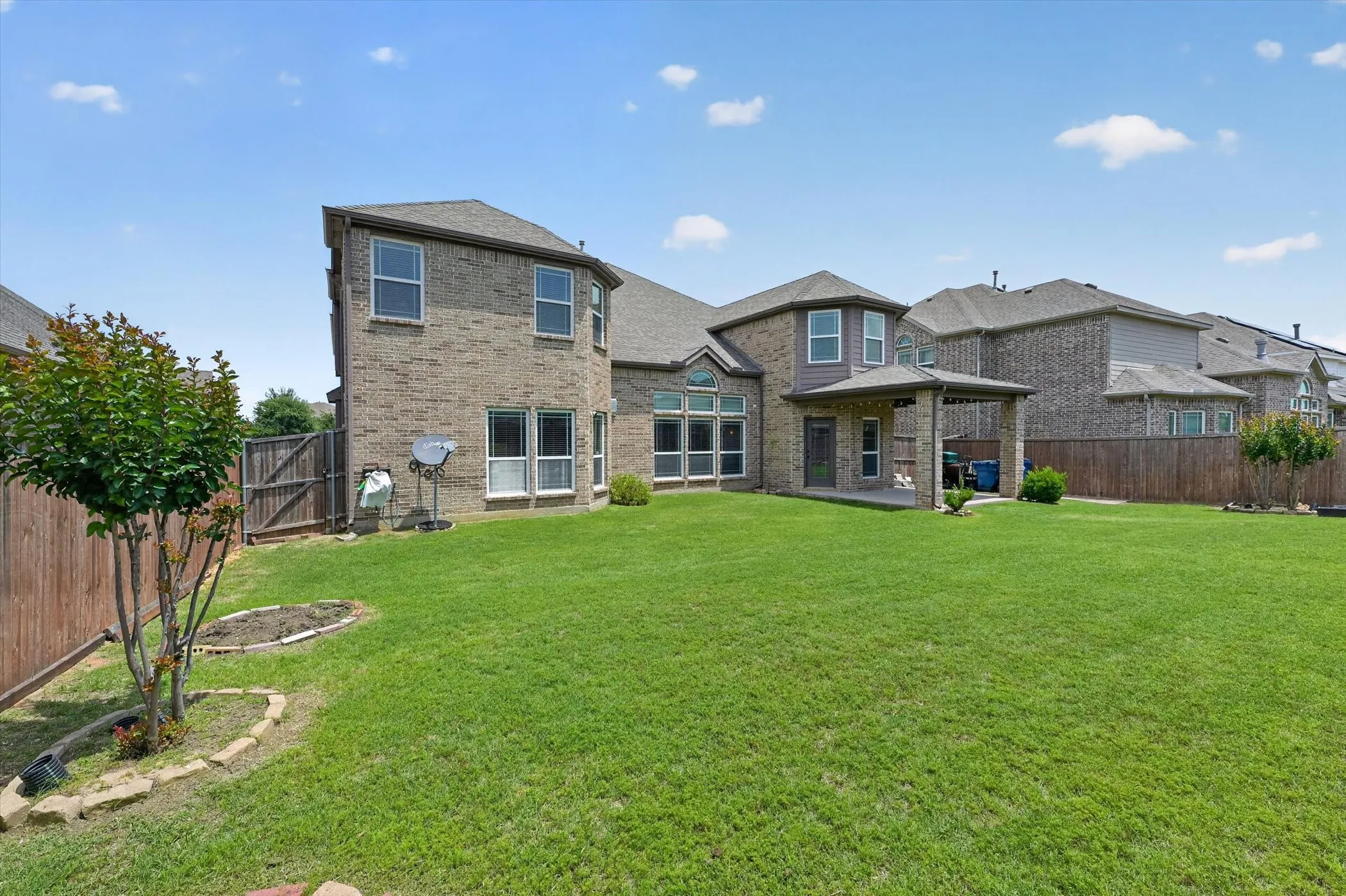 Expansive rear yard featuring a large green lawn, a covered patio, and a privacy fence