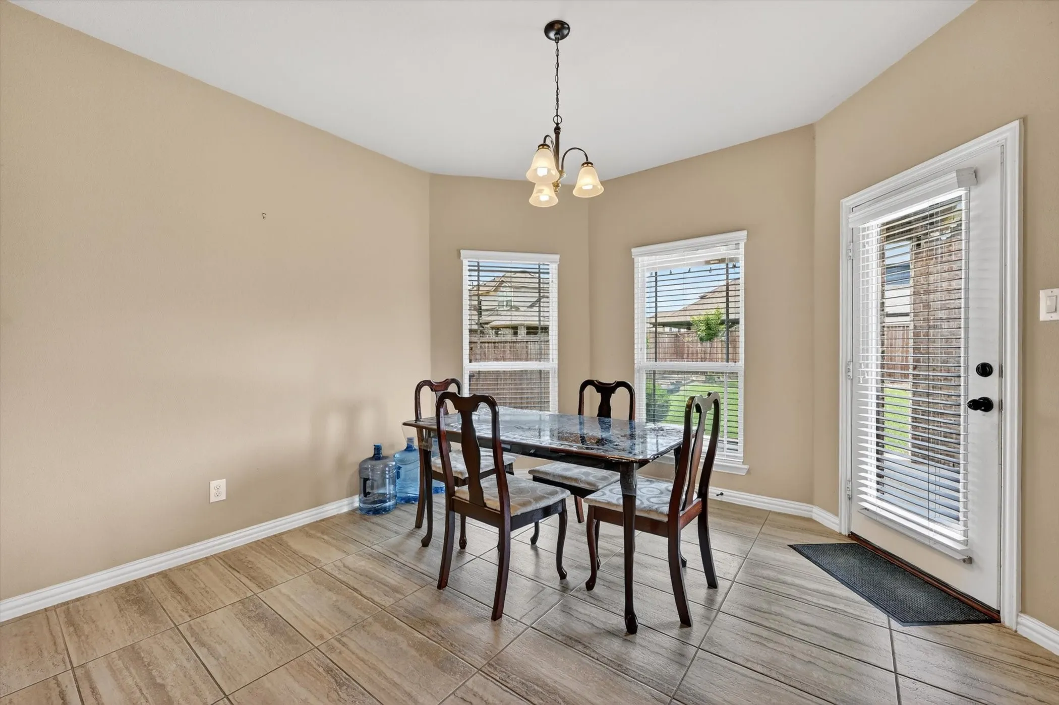 Dining area featuring neutral wall tones, tile flooring, two windows with blinds, a white exterior door with internal blinds, and a multi-bulb ceiling fixture