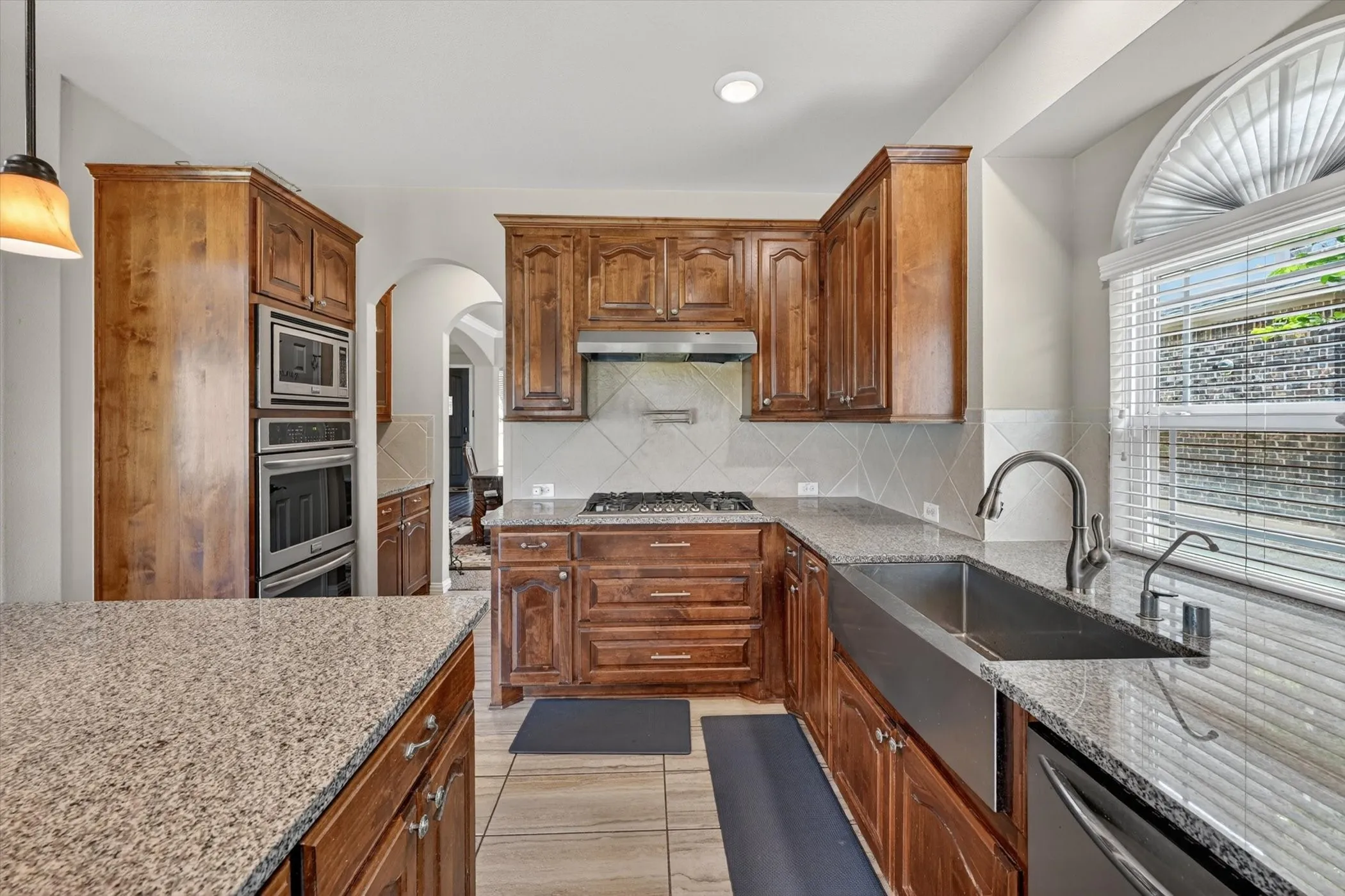 Kitchen featuring granite countertops, wood cabinetry, stainless steel appliances, and a farmhouse sink