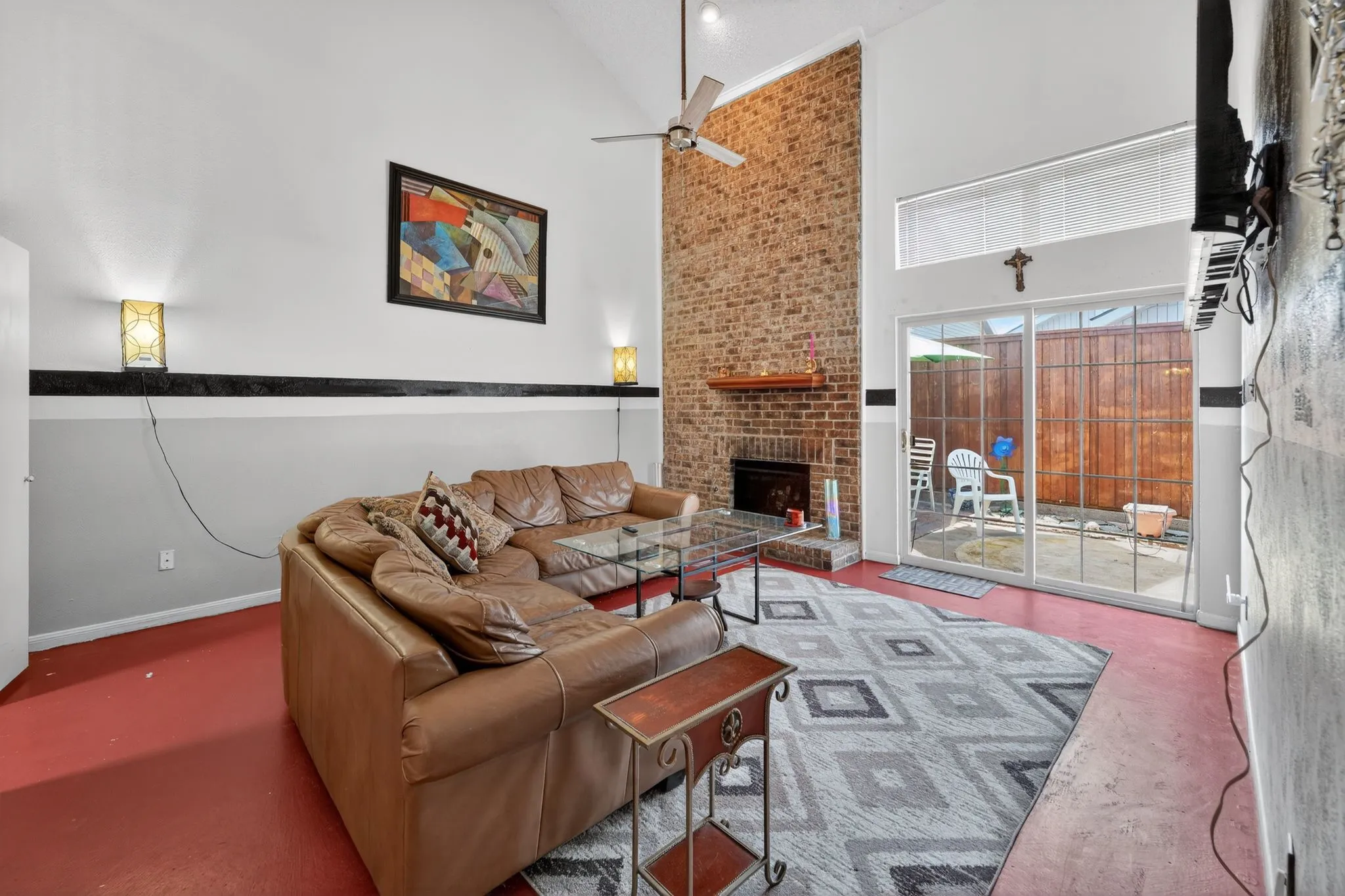 Vaulted ceiling living area featuring a brick fireplace with wood mantel, ceiling fan, and sliding glass doors to a private patio