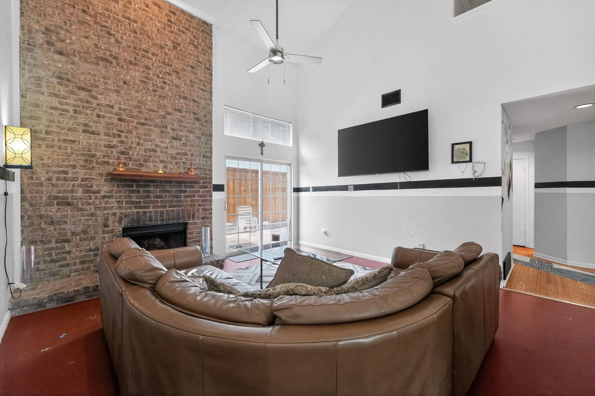 Living area featuring a floor-to-ceiling exposed brick fireplace with a wood mantle, vaulted ceilings, and a ceiling fan