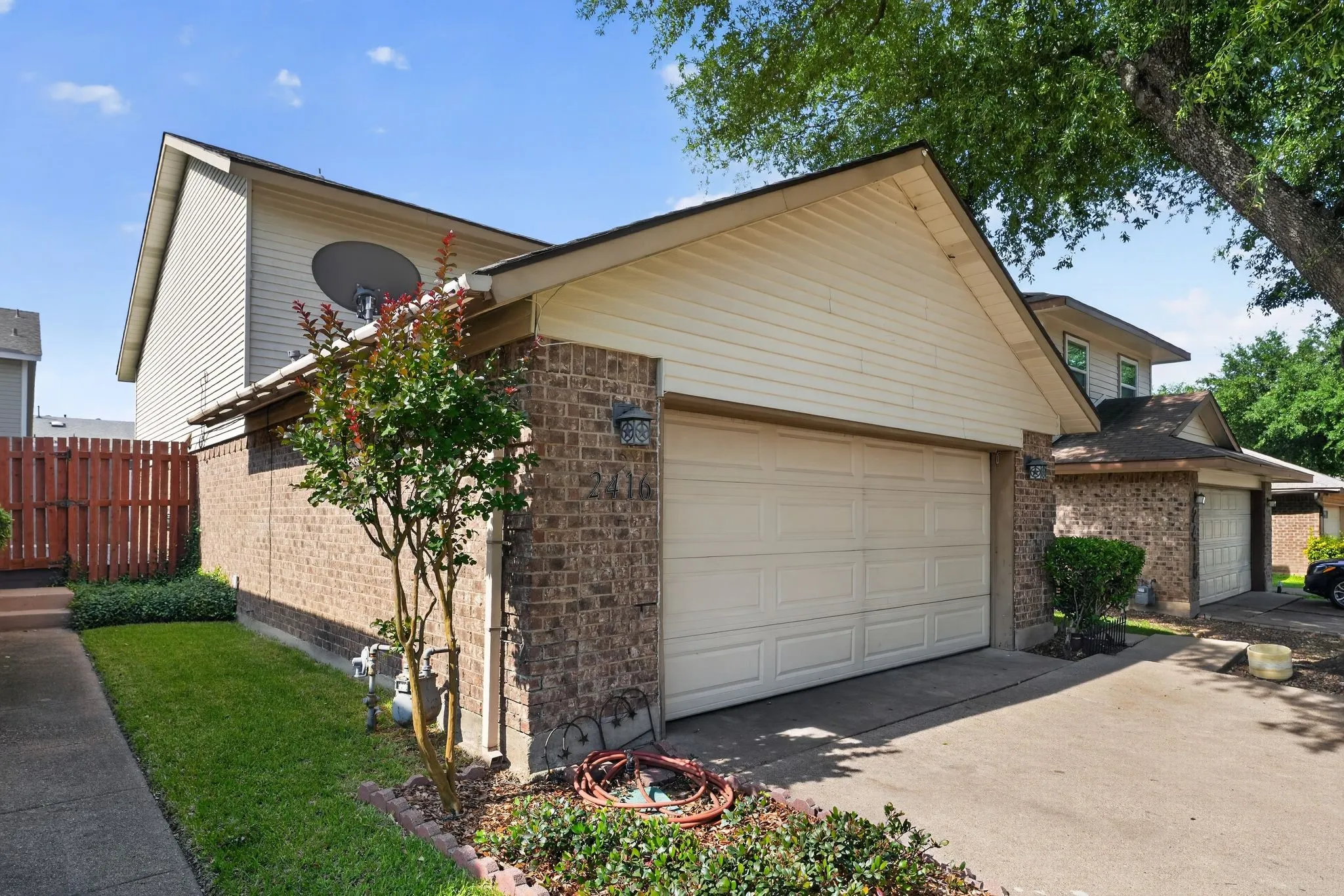 Brick facade two-story residence featuring a two-car garage with a panel door, gabled roofline, and mature trees