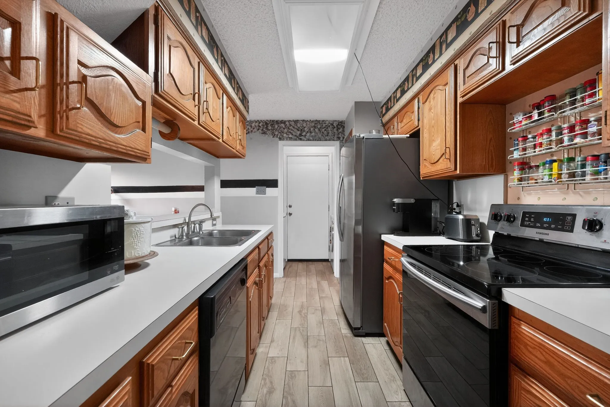 Galley kitchen featuring wood cabinetry, light countertops, wood-finish flooring, a stainless steel sink, and modern appliances