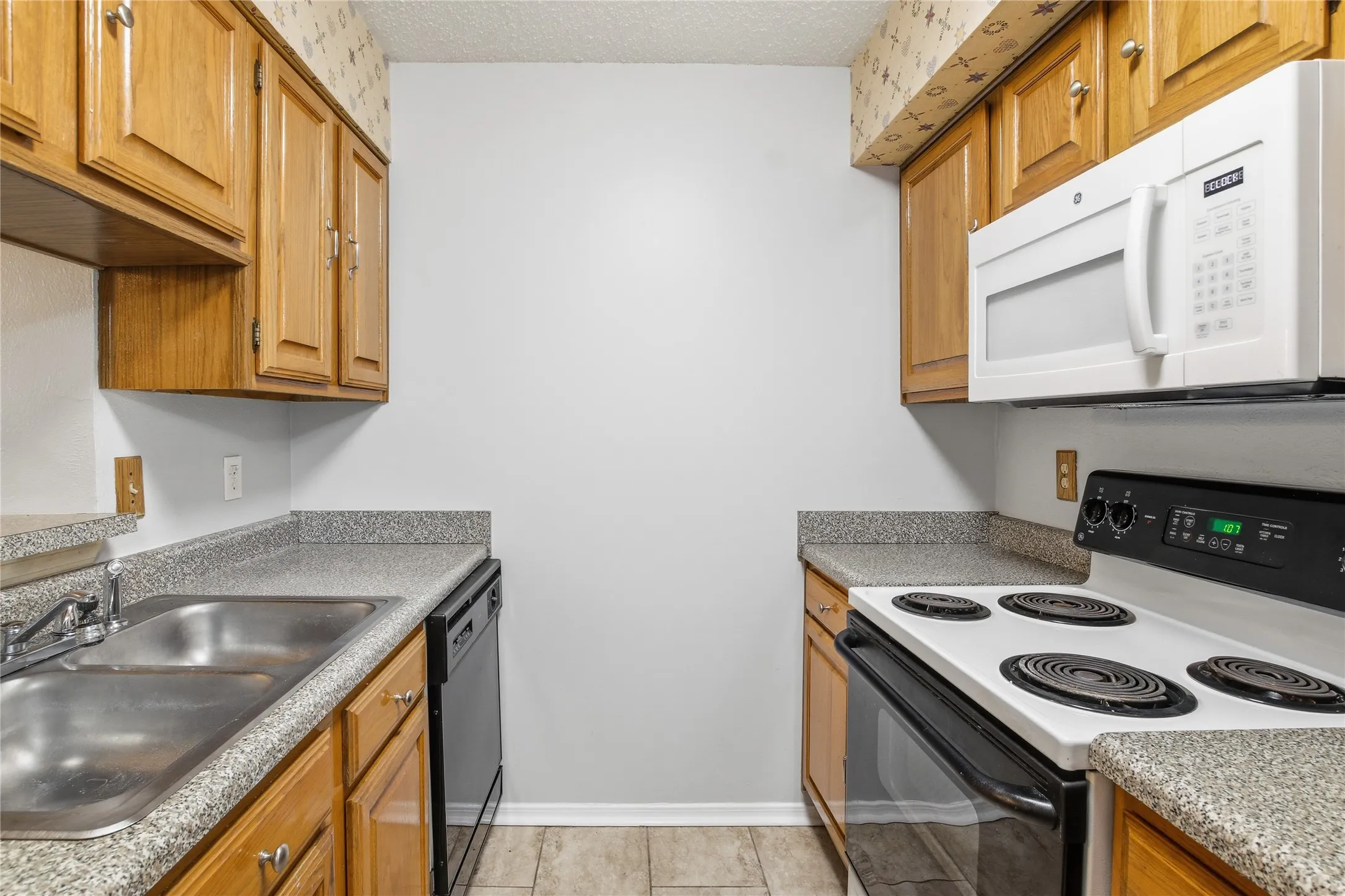 Galley kitchen featuring wood cabinetry, stone-finish countertops, and tile flooring