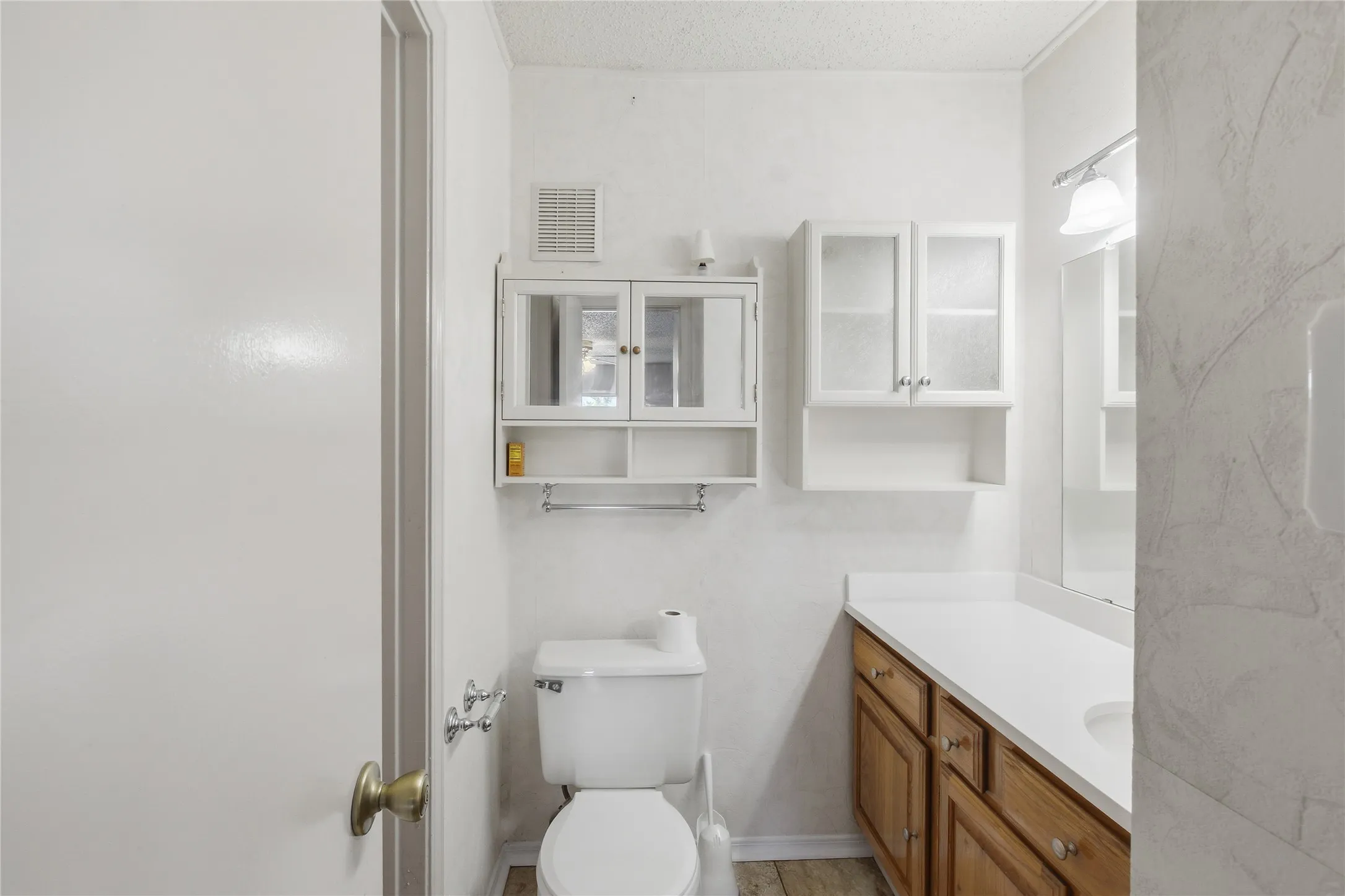 Bathroom featuring a white toilet, wood-finish vanity with an integrated sink, white countertop, and wall-mounted storage cabinets