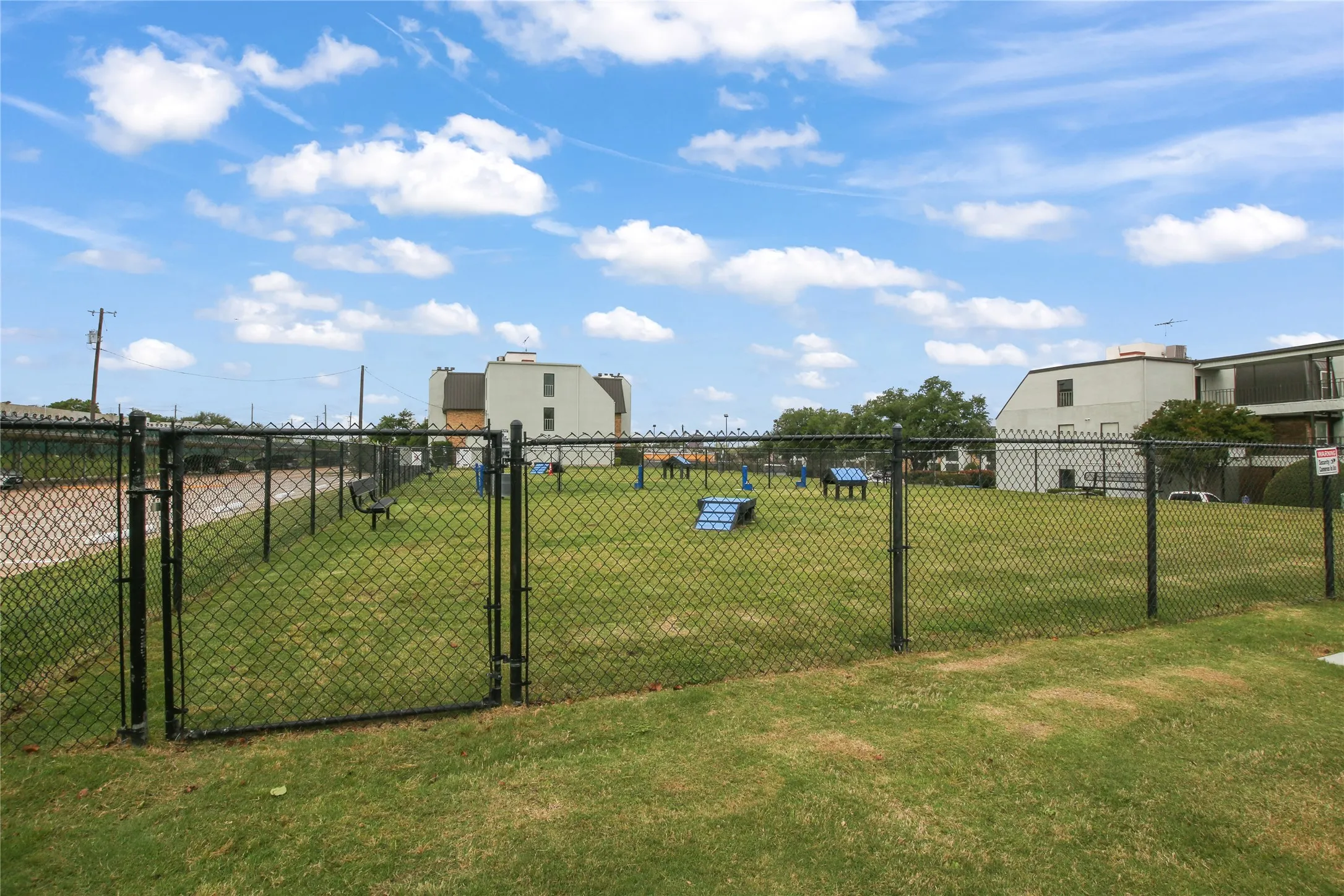 Fenced outdoor area featuring a grass lawn, agility equipment, and a dedicated entry gate