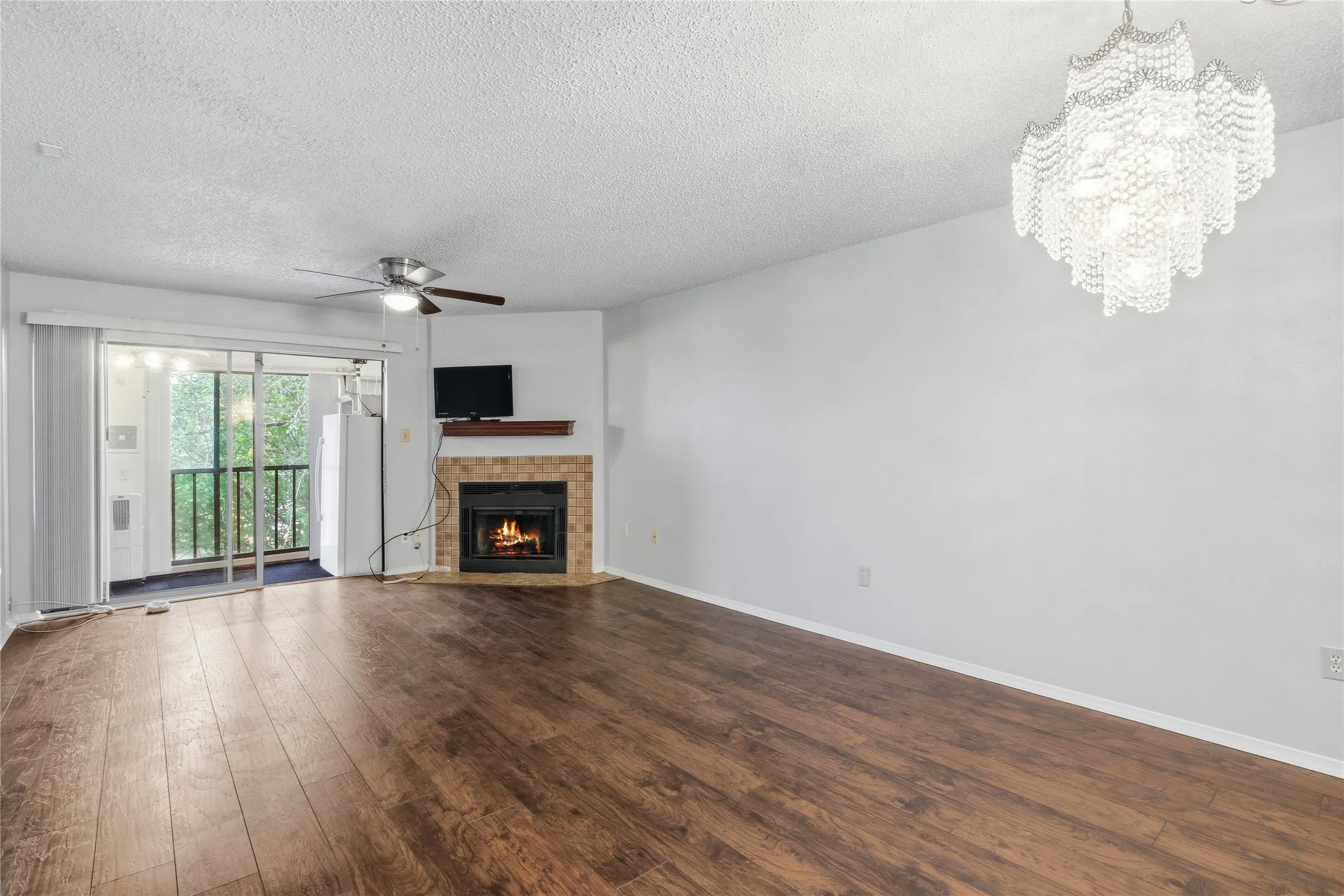 Spacious living area featuring wood-finish flooring, a corner fireplace with a tiled surround, and a decorative chandelier