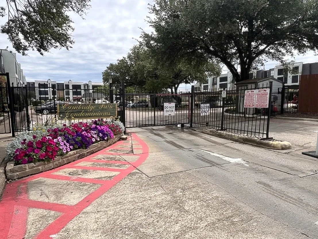 Gated entry to Cambridge Park Condominiums, featuring a stone-faced planter with vibrant mixed perennial flowers