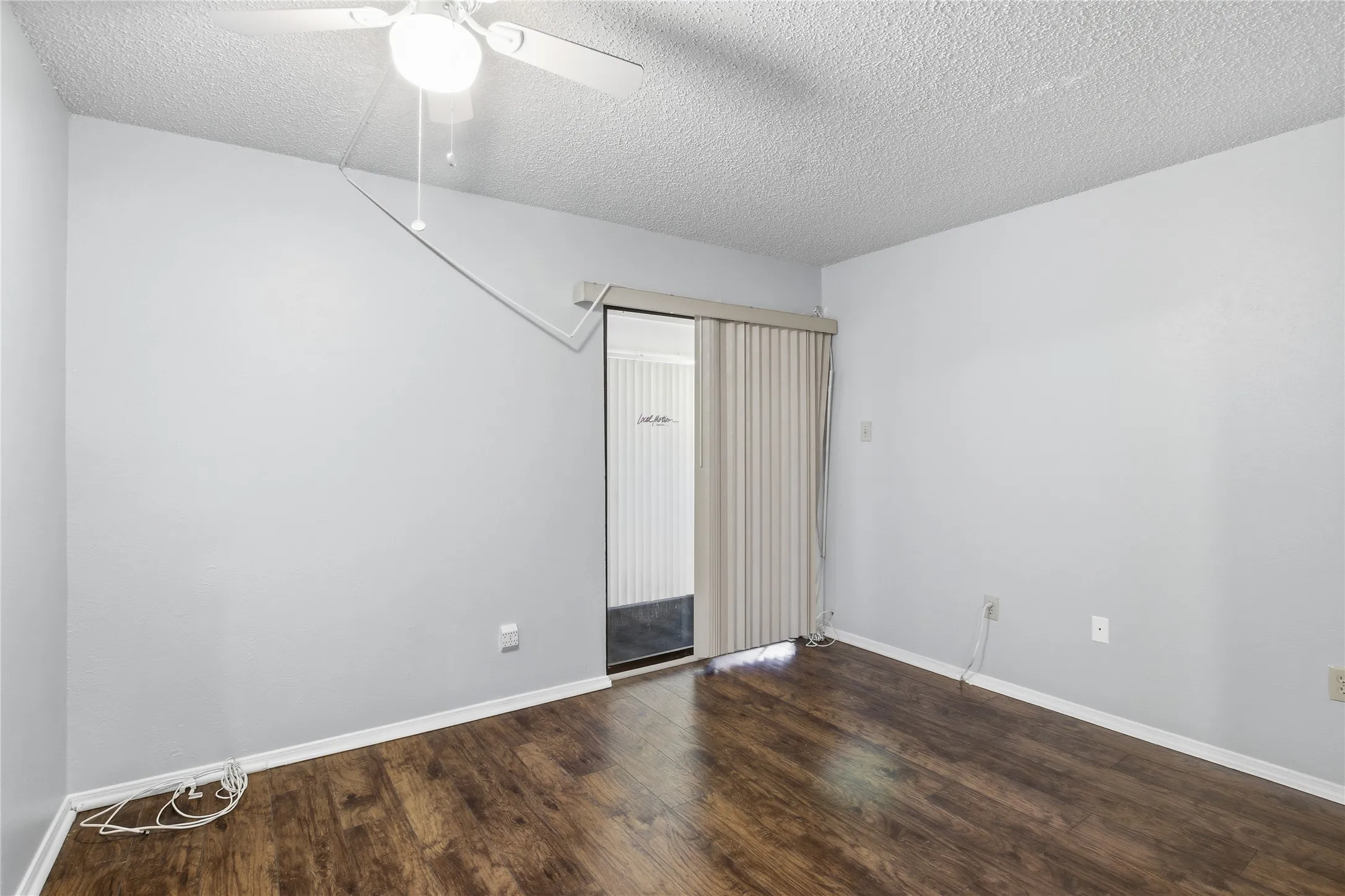 Room featuring wood-finish flooring, light gray walls, white trim, and a ceiling fan with integrated lighting