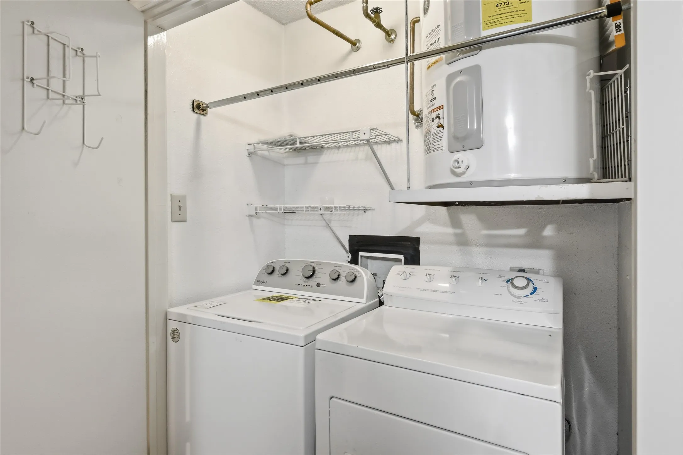 Dedicated laundry area featuring a white washing machine and dryer, overhead shelving, and a water heater