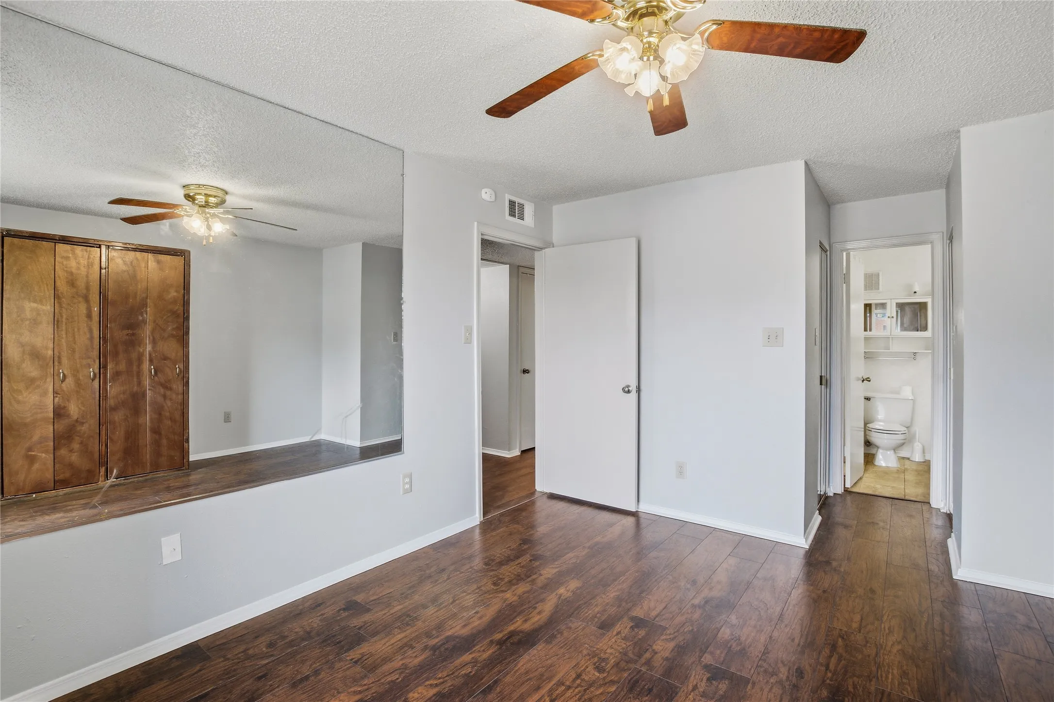 Interior space featuring wood-finish flooring, a wall-mounted mirror, a ceiling fan with light fixture, and a built-in wood-paneled wardrobe
