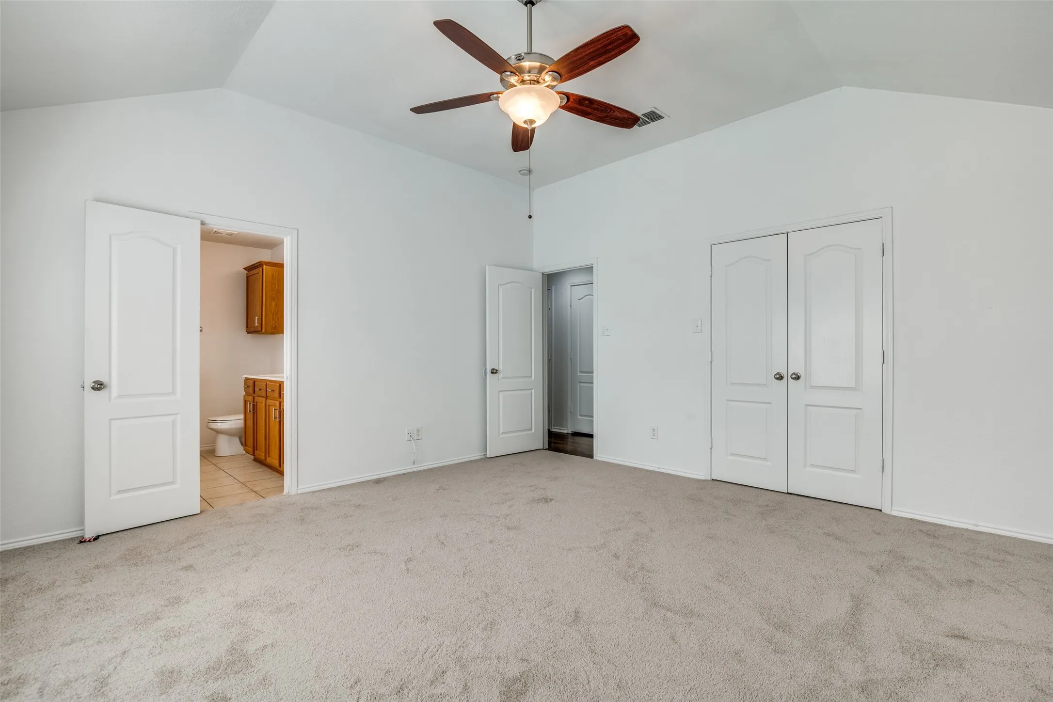 Unfurnished bedroom with ensuite bath, light carpet, vaulted ceiling, and ceiling fan