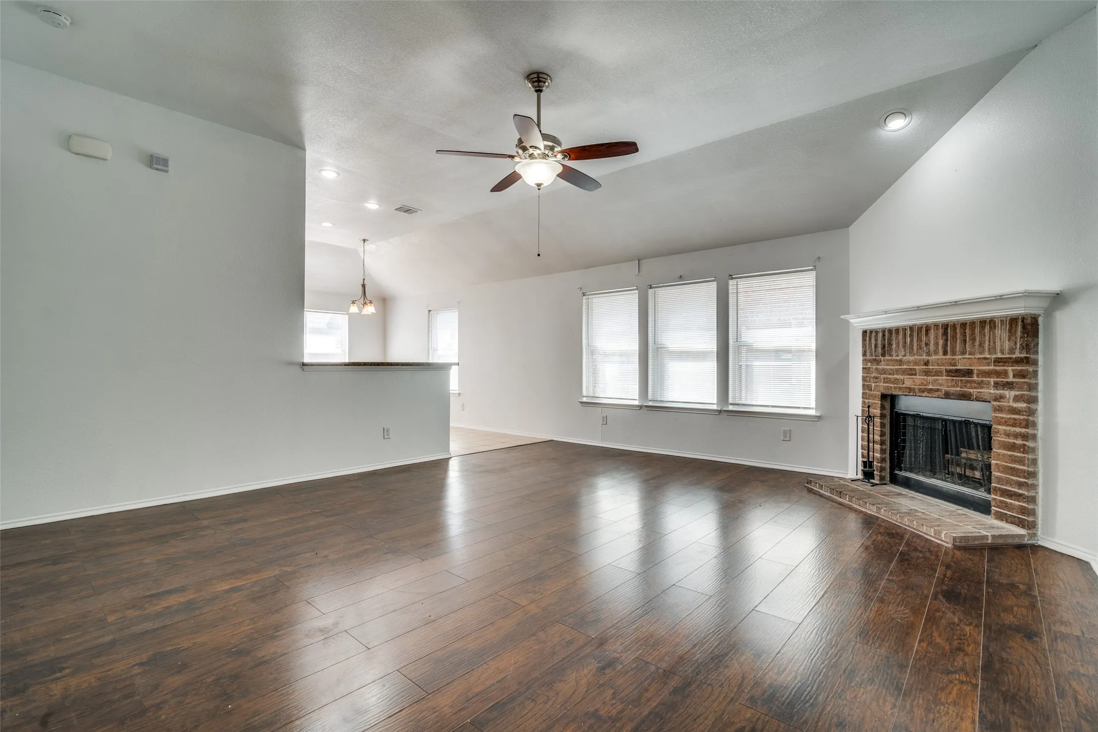 Unfurnished living room featuring ceiling fan with notable chandelier, a fireplace, lofted ceiling, and dark hardwood / wood-style floors