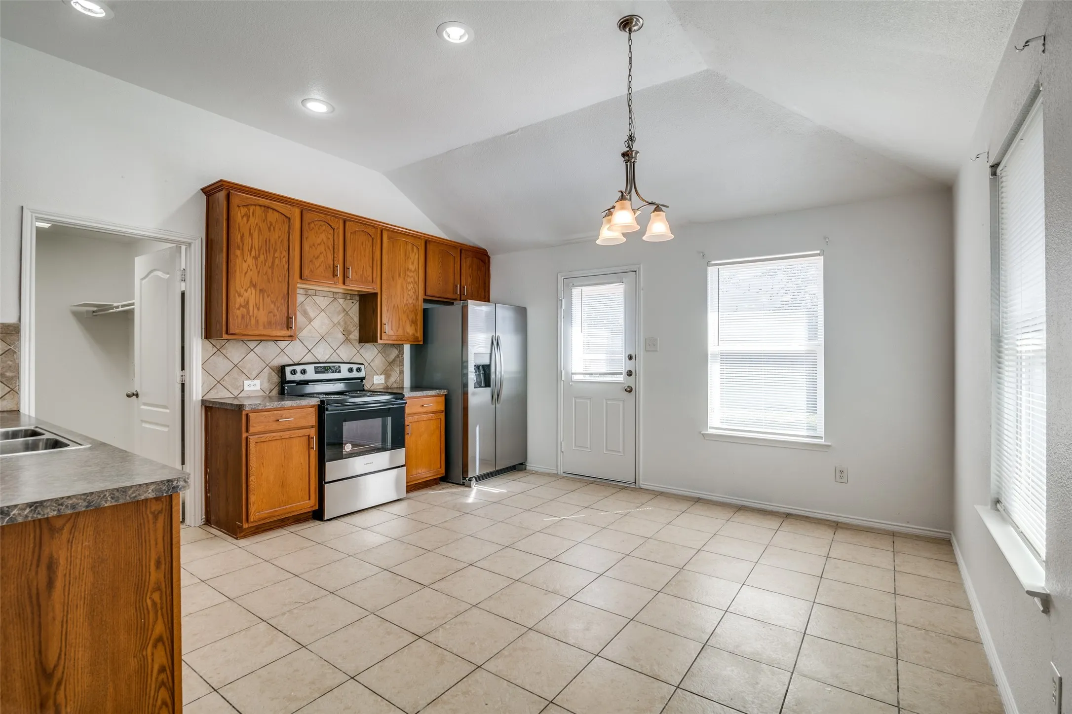 Kitchen featuring light tile patterned flooring, backsplash, hanging light fixtures, stainless steel appliances, and vaulted ceiling