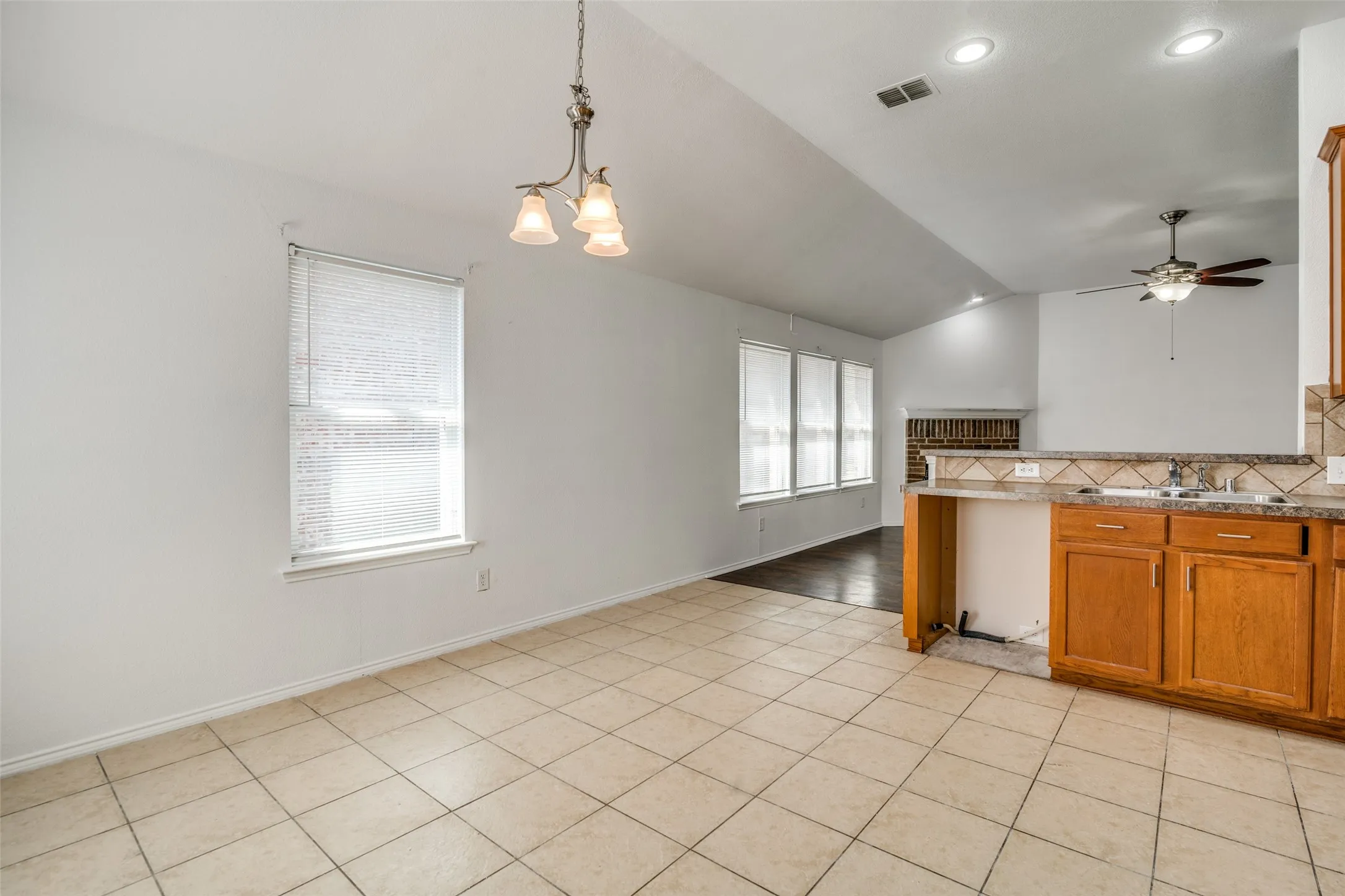 Kitchen featuring backsplash, sink, vaulted ceiling, pendant lighting, and light tile patterned floors