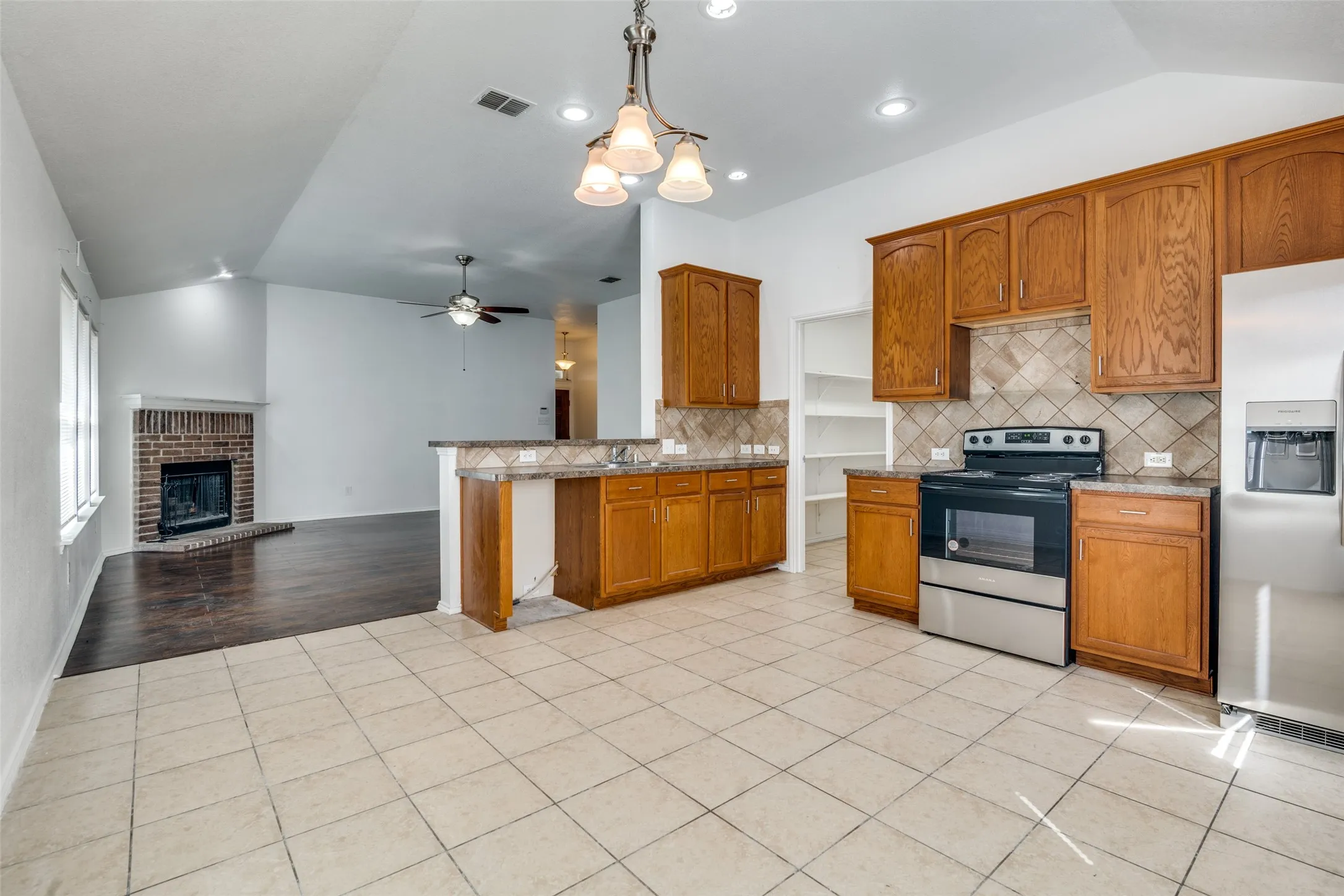 Kitchen with light wood-type flooring, a fireplace, ceiling fan with notable chandelier, stainless steel appliances, and pendant lighting