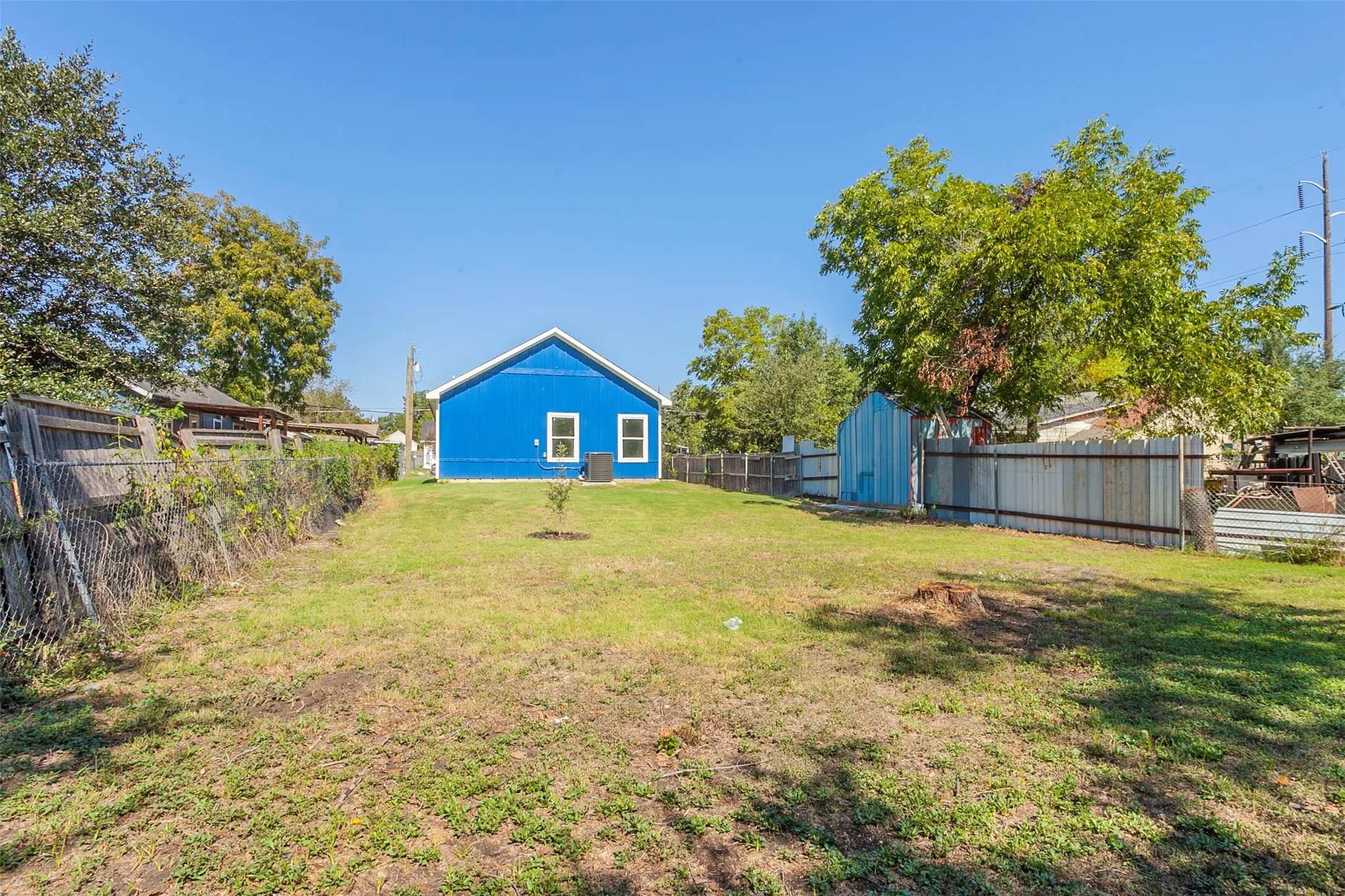Spacious backyard featuring a blue exterior dwelling, mature trees, and a combination of chain-link and privacy fencing