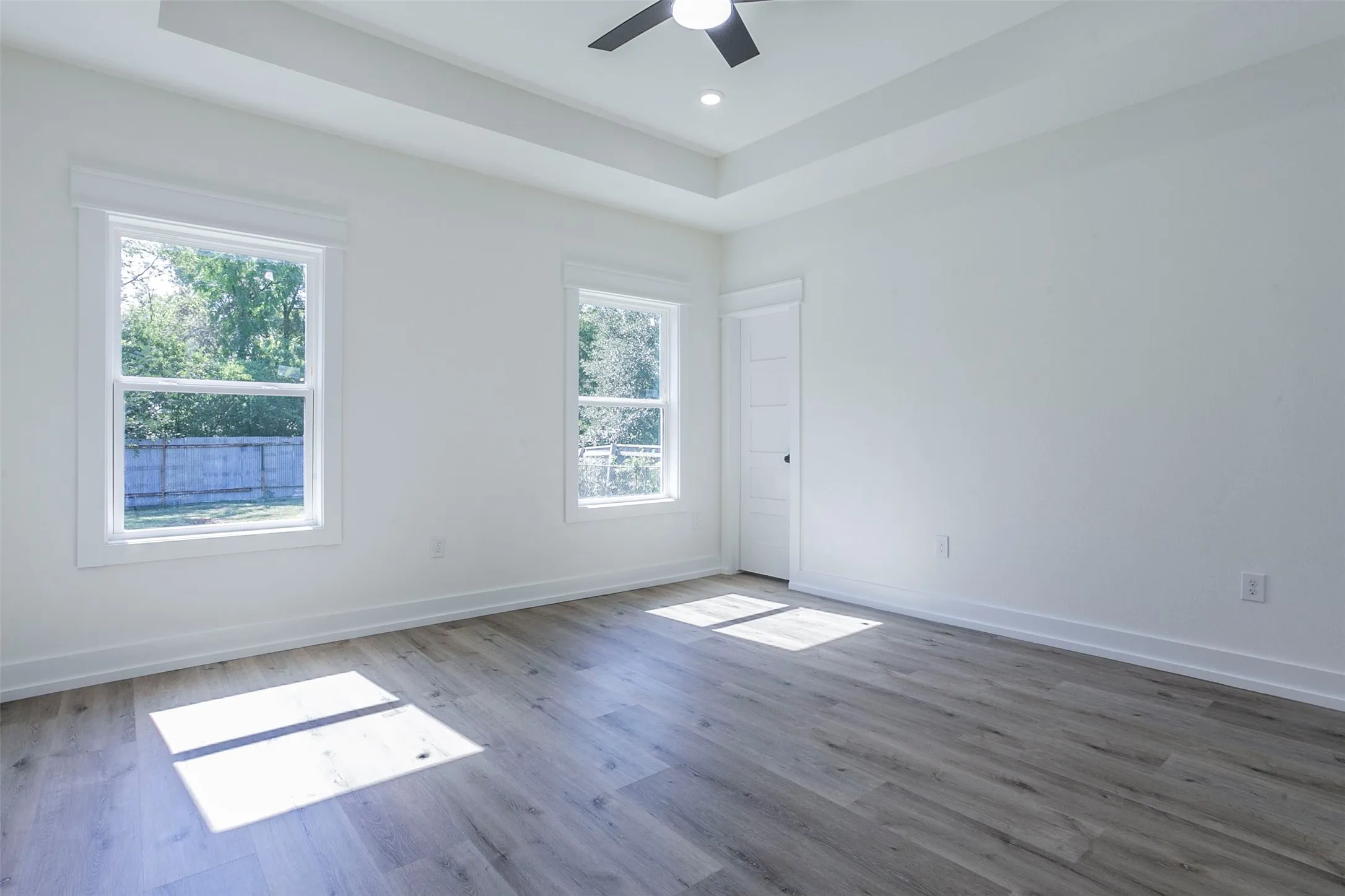 Room with wood-finish flooring, white walls, and a tray ceiling