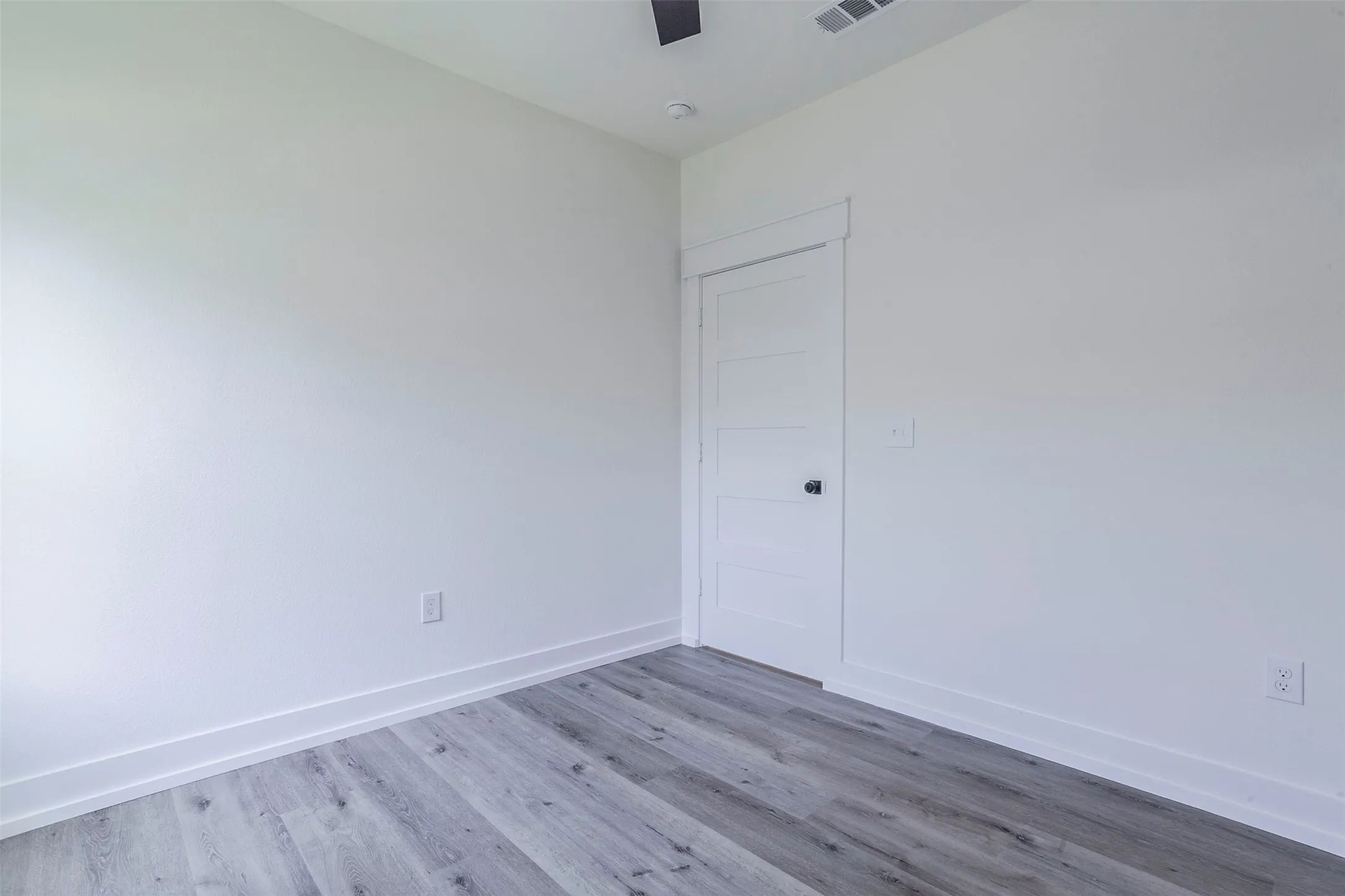 Light-filled room featuring wood-finish flooring, white baseboards, and a contemporary flat-panel door with black hardware
