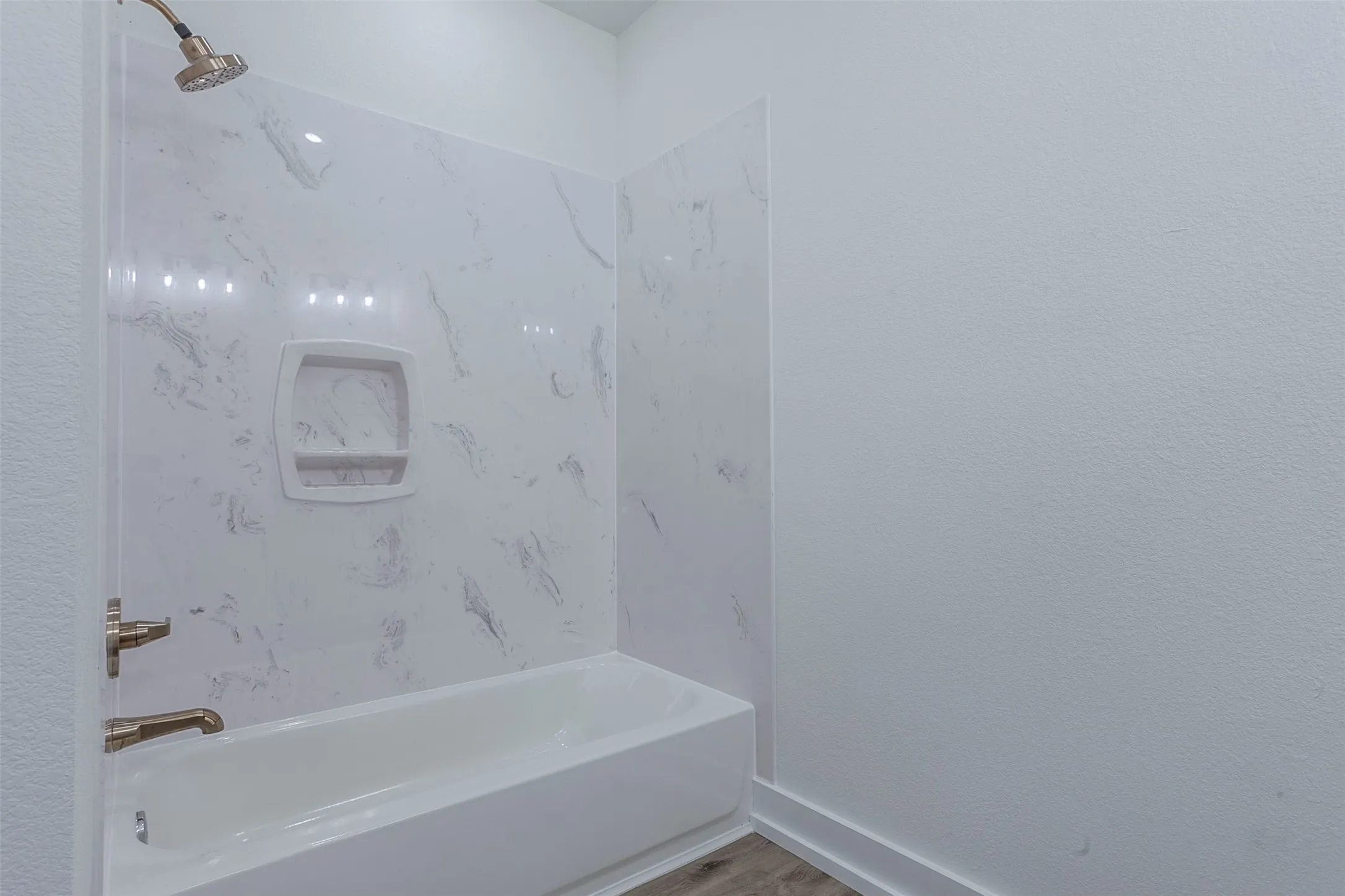 Bathroom featuring a white tub, white faux-marble shower surround, integrated shower niche, and brushed brass fixtures