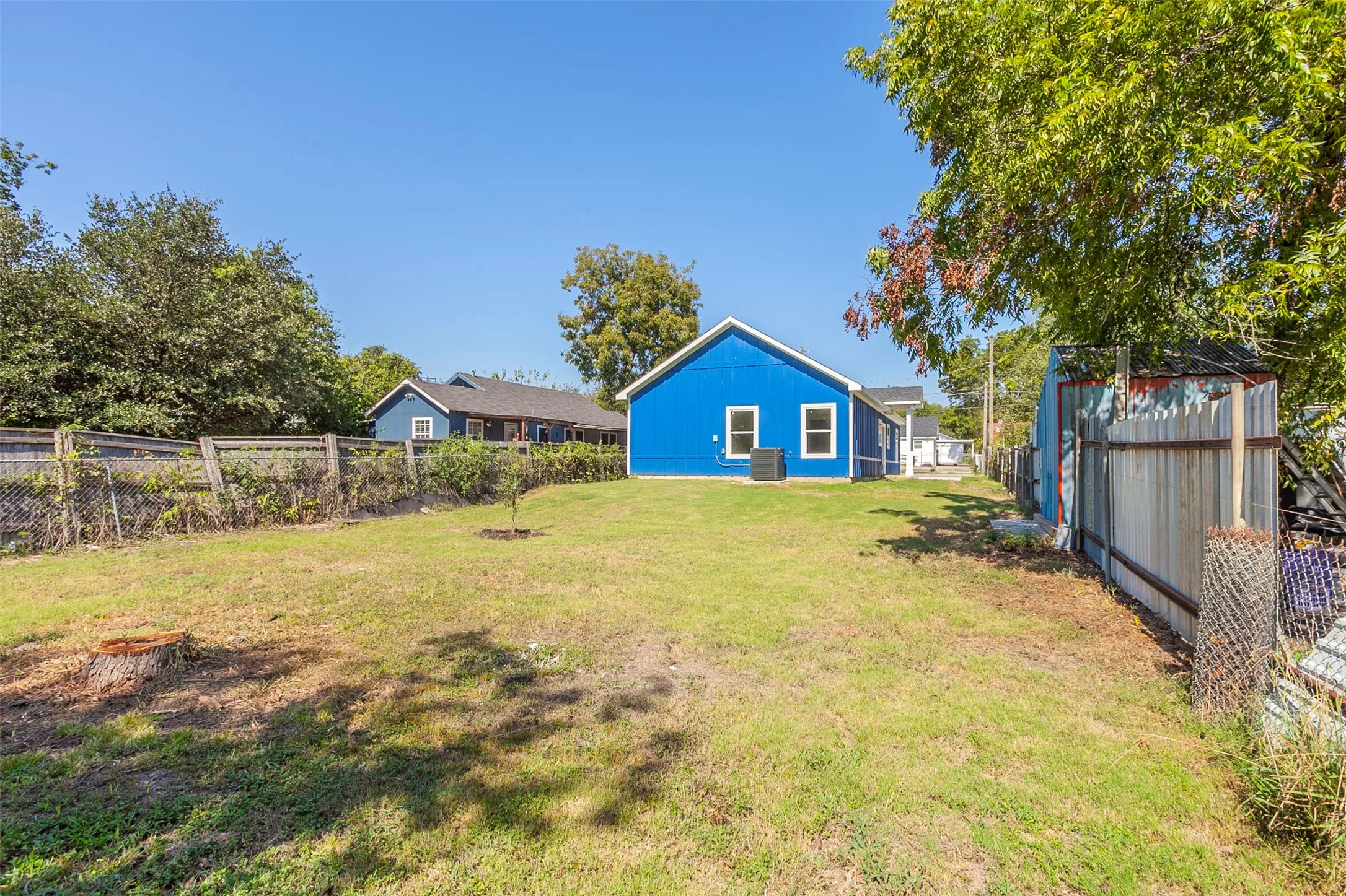 Expansive backyard featuring a manicured lawn, established trees, and a chain-link fence