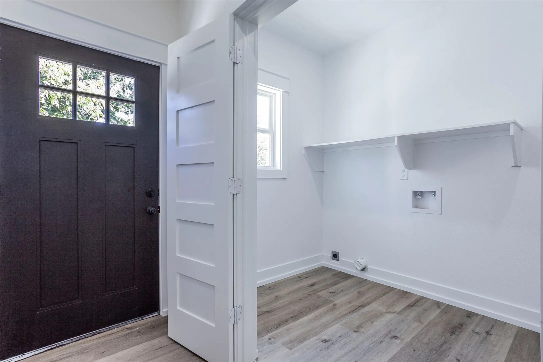 Utility space featuring wood-finish flooring, white walls, and a built-in storage shelf