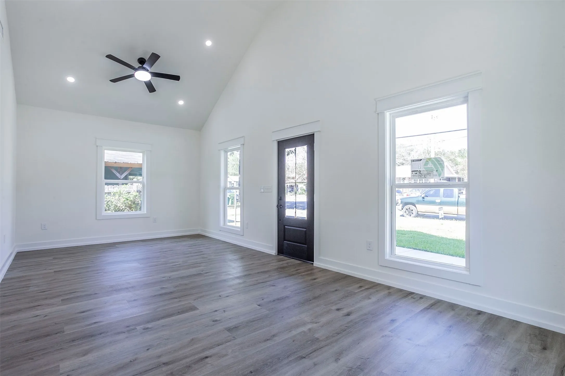 Spacious interior featuring a vaulted ceiling with a ceiling fan, recessed lighting, wood-finish flooring, white baseboards, and white window trim