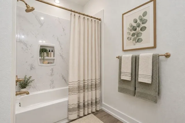 Virtual staging -Bathtub with a built-in shower niche, brushed bronze fixtures, and a white marble-look shower surround