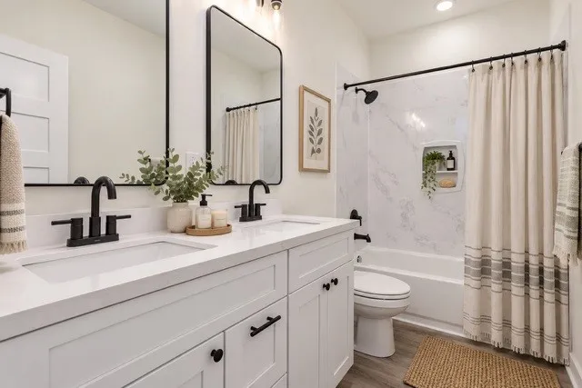 Virtual staging - Double vanity with white cabinetry and integrated sinks, matte black fixtures, framed mirrors, and a shower-over-tub with a built-in niche