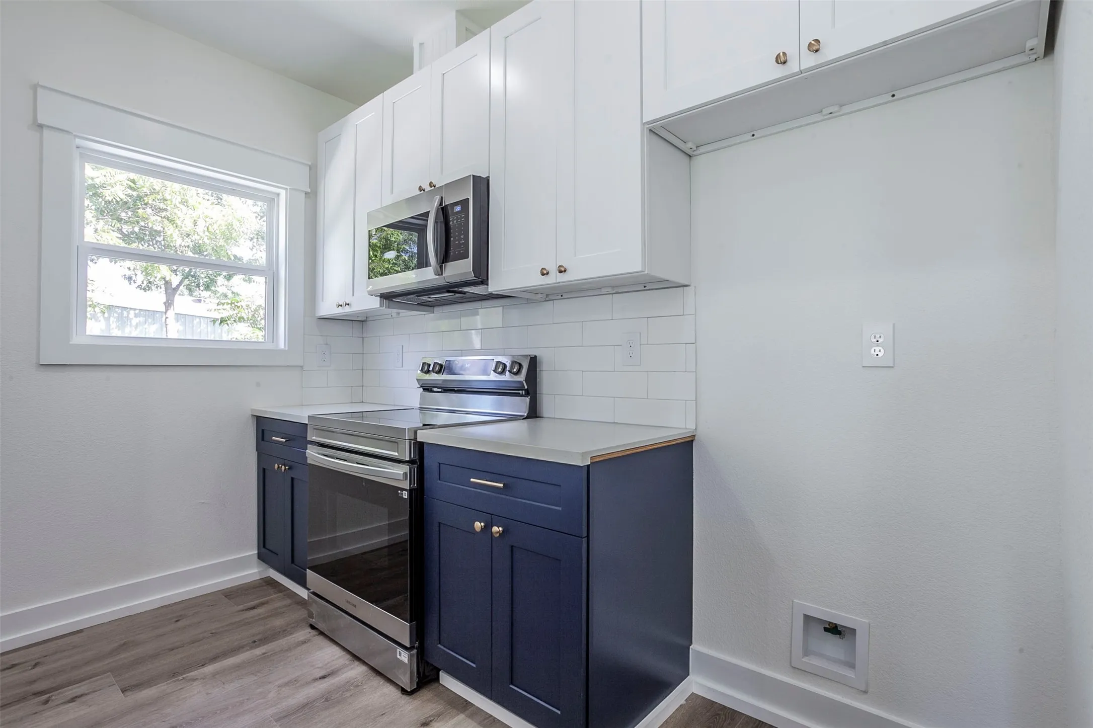 Modern kitchen featuring two-tone cabinetry with white upper and navy lower cabinets, stainless steel appliances, a white subway tile backsplash, and light wood-finish flooring