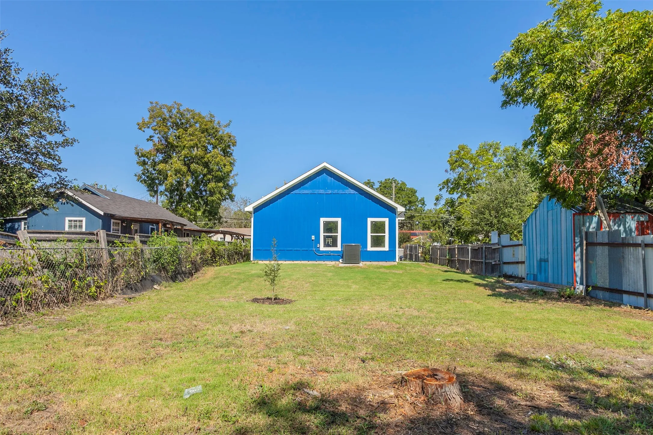 Spacious backyard featuring a vibrant blue exterior, white trim windows, and mature trees