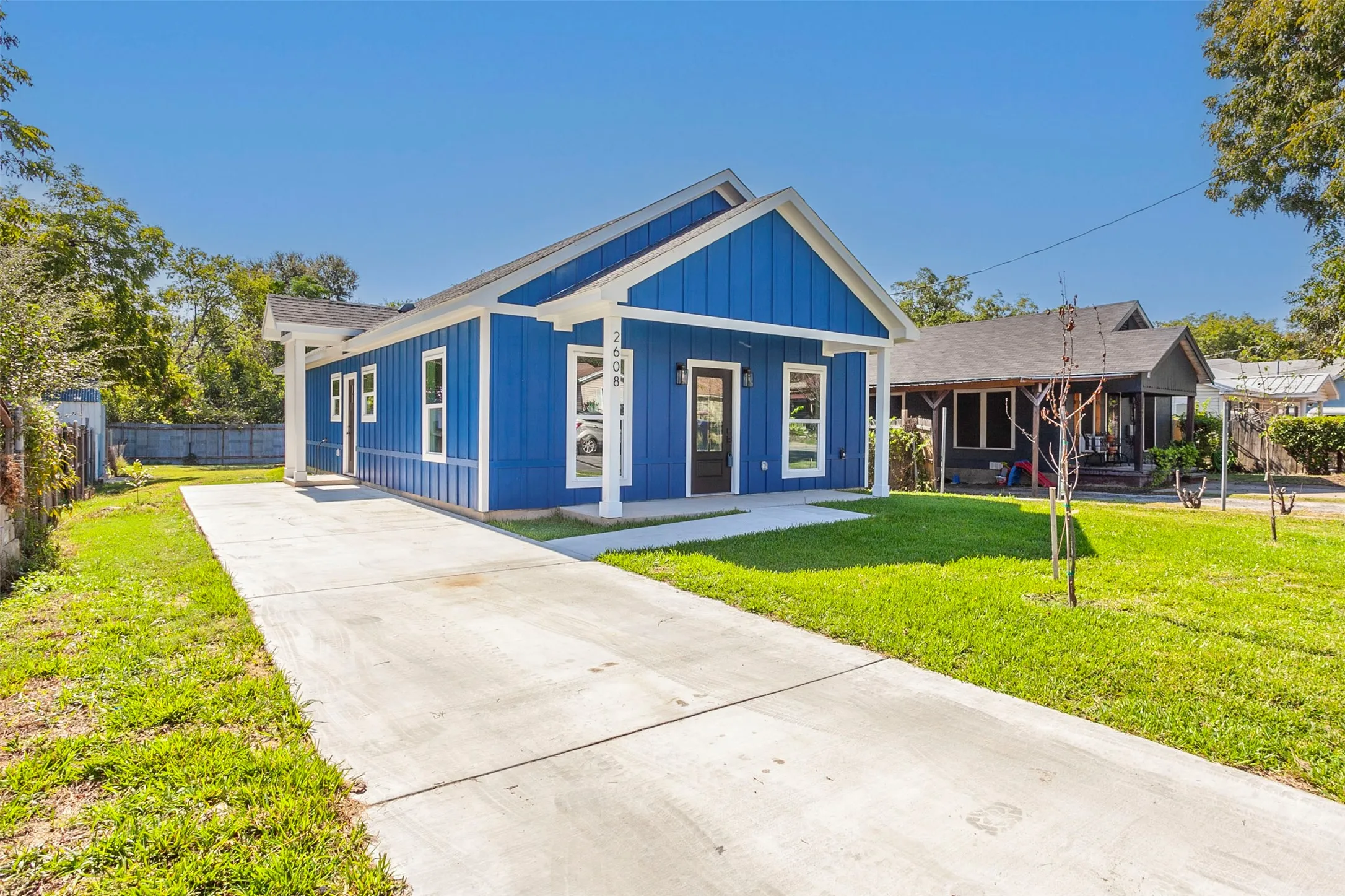 Bright blue exterior siding with white trim, a covered front porch, a concrete driveway, a front lawn, and mature trees in the background
