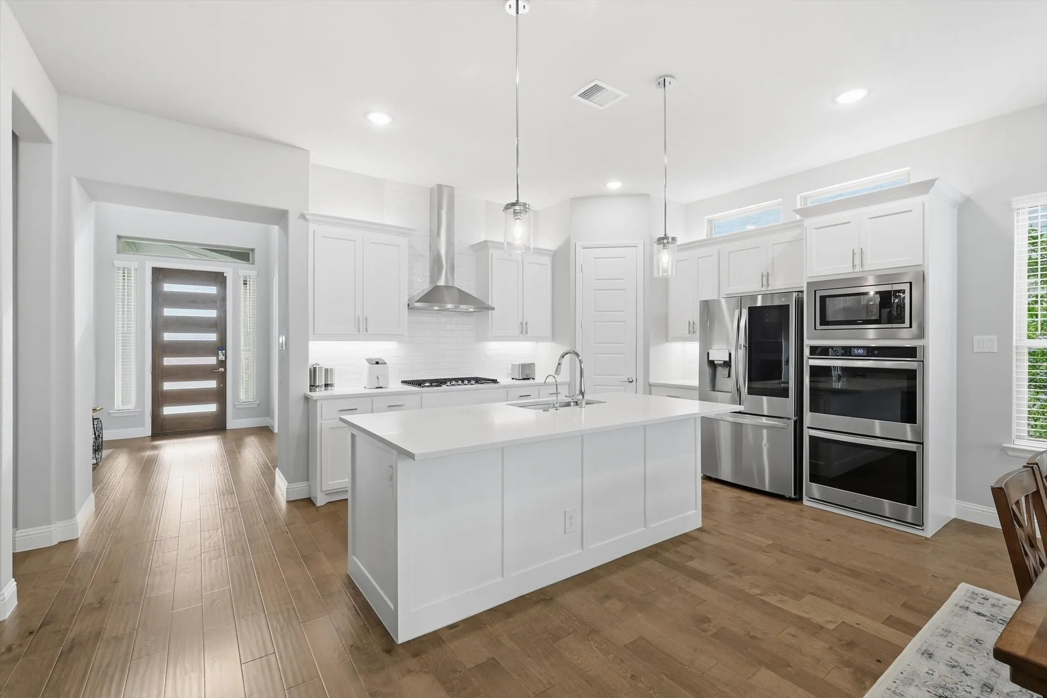 Chef inspired kitchen is designed to impress, showcasing custom cabinetry with designer hardware, an oversized quartz island, stainless steel appliances, a 5 burner gas cooktop with double ovens, custom backsplash, vent hood, and a spacious walk-in pantry!