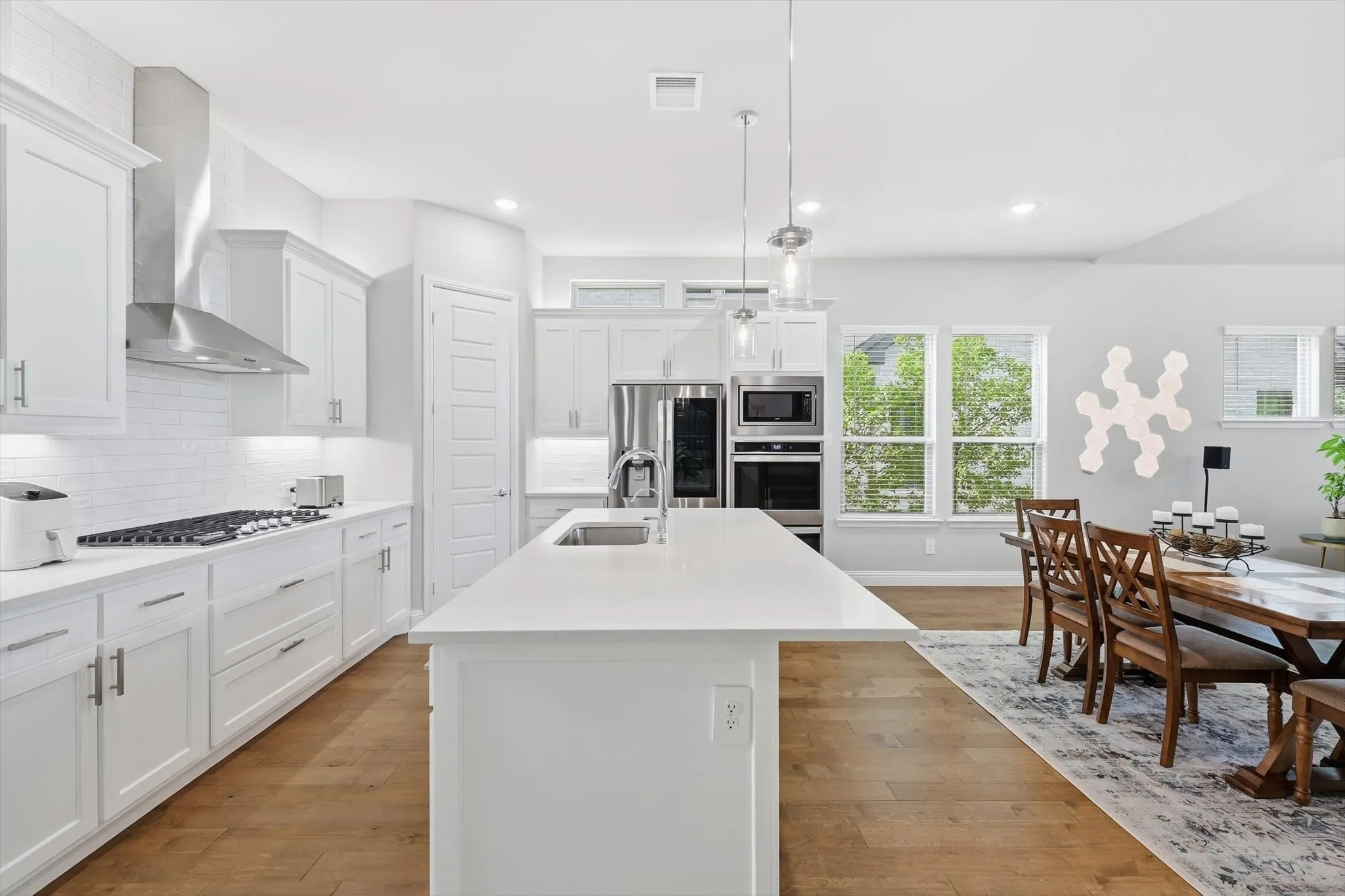 Chef inspired kitchen is designed to impress, showcasing custom cabinetry with designer hardware, an oversized quartz island, stainless steel appliances, a 5 burner gas cooktop with double ovens, custom backsplash, vent hood, and a spacious walk-in pantry!