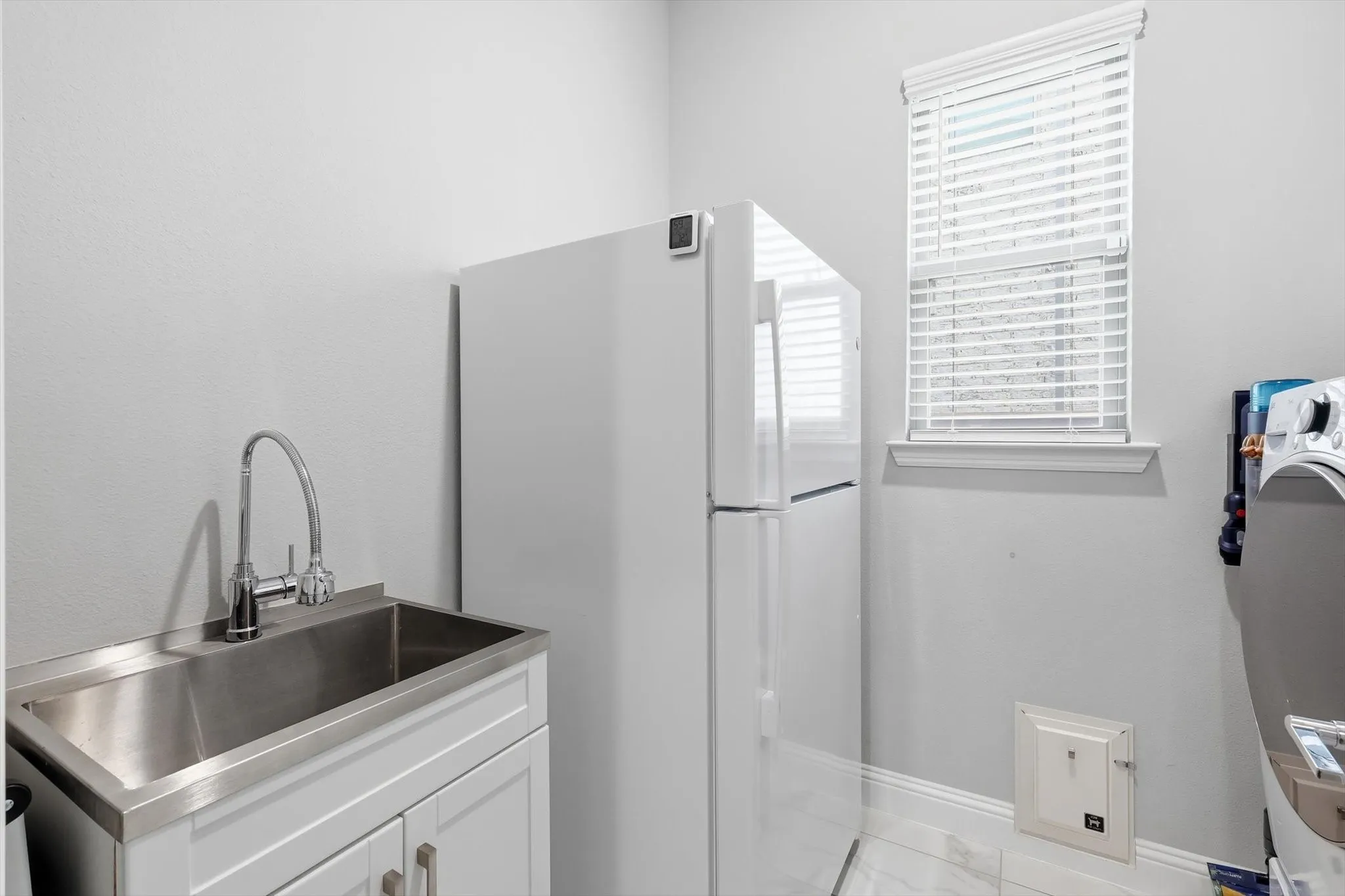 Spacious laundry room includes a sink & room for another refrigerator.
